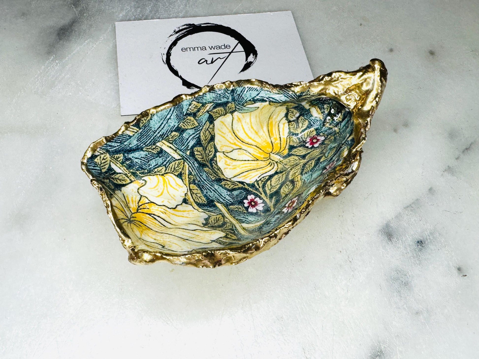 William Morris Golden Green Pimpernel oyster shell ring dish with gold leaf edge. A unique shell ring holder, ring tray, and jewellery organiser for rings, earrings, or cufflinks. Each shell features an art inspired floral design and is individually handmade from Dorset shells. Perfect as a trinket dish for bedside or dressing table storage. A thoughtful gift for weddings, anniversaries, birthdays, bridesmaids, or Christmas. A sustainable decorative keepsake for any jewellery lover.
