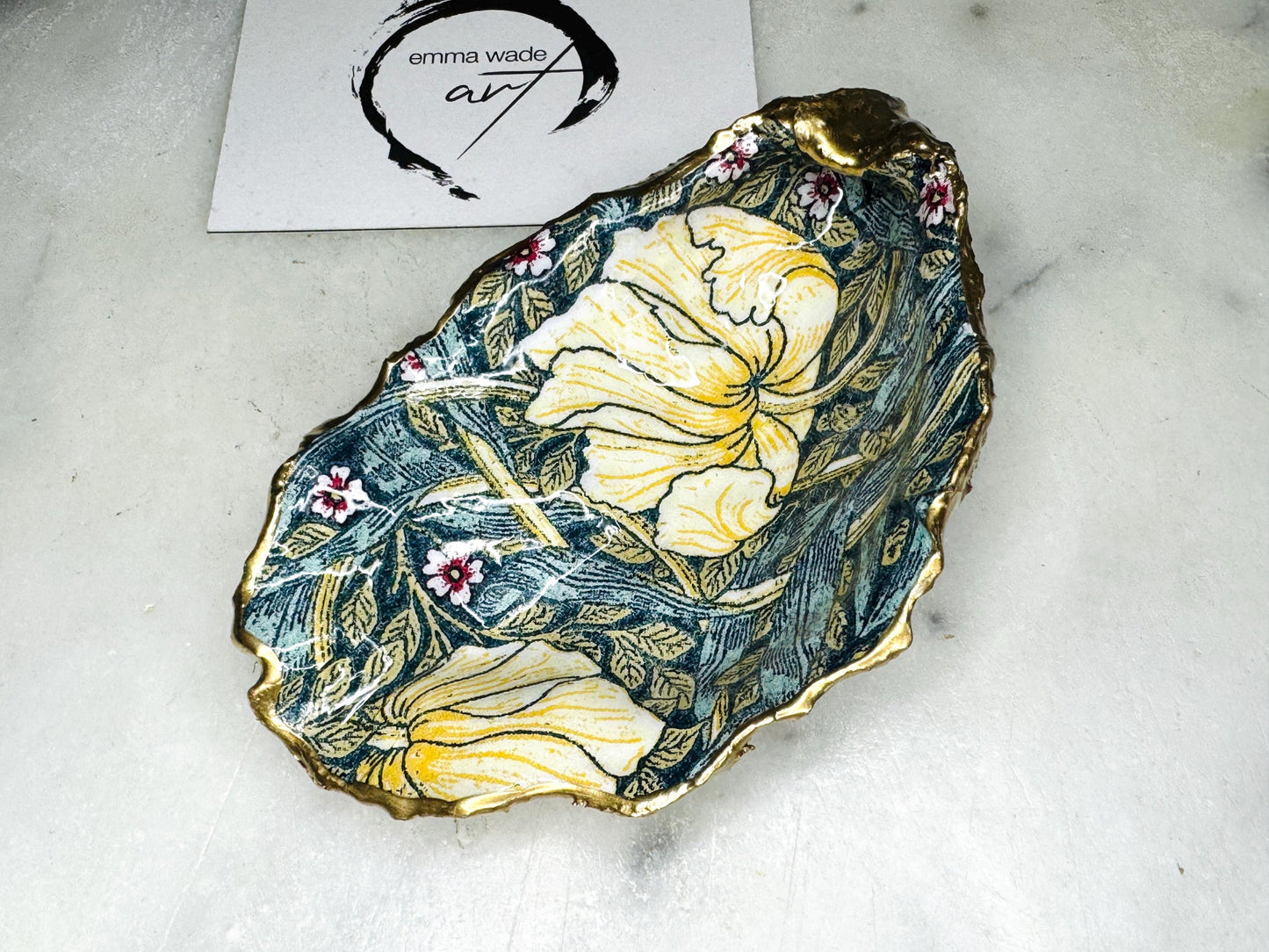 William Morris Golden Green Pimpernel oyster shell ring dish with gold leaf edge. A unique shell ring holder, ring tray, and jewellery organiser for rings, earrings, or cufflinks. Each shell features an art inspired floral design and is individually handmade from Dorset shells. Perfect as a trinket dish for bedside or dressing table storage. A thoughtful gift for weddings, anniversaries, birthdays, bridesmaids, or Christmas. A sustainable decorative keepsake for any jewellery lover.