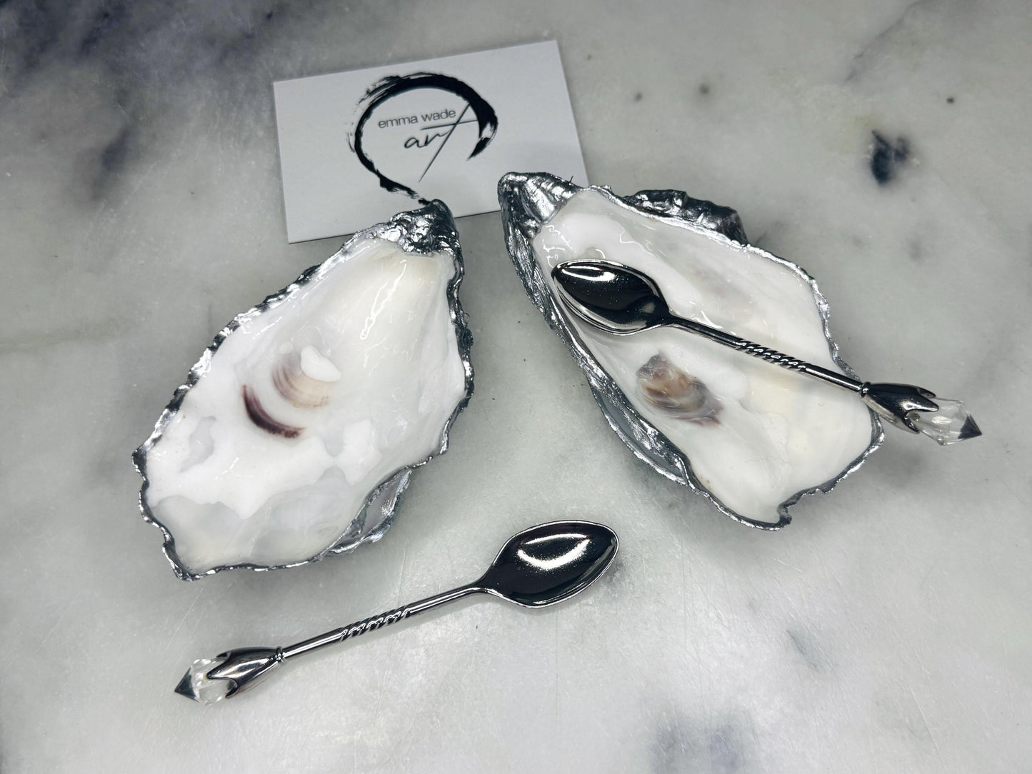 Handmade pearl oyster shell salt and pepper pinch pots with silver leaf accents and optional crystal spoons. Coastal tableware set made from natural Dorset oyster shells, polished to a natural white pearl finish and sealed with food-safe glossy resin. Elegant shell salt dishes photographed on a light background, showing two domed shells with matching bases, ideal for serving salt, pepper or spices at stylish dinner tables and special occasions.