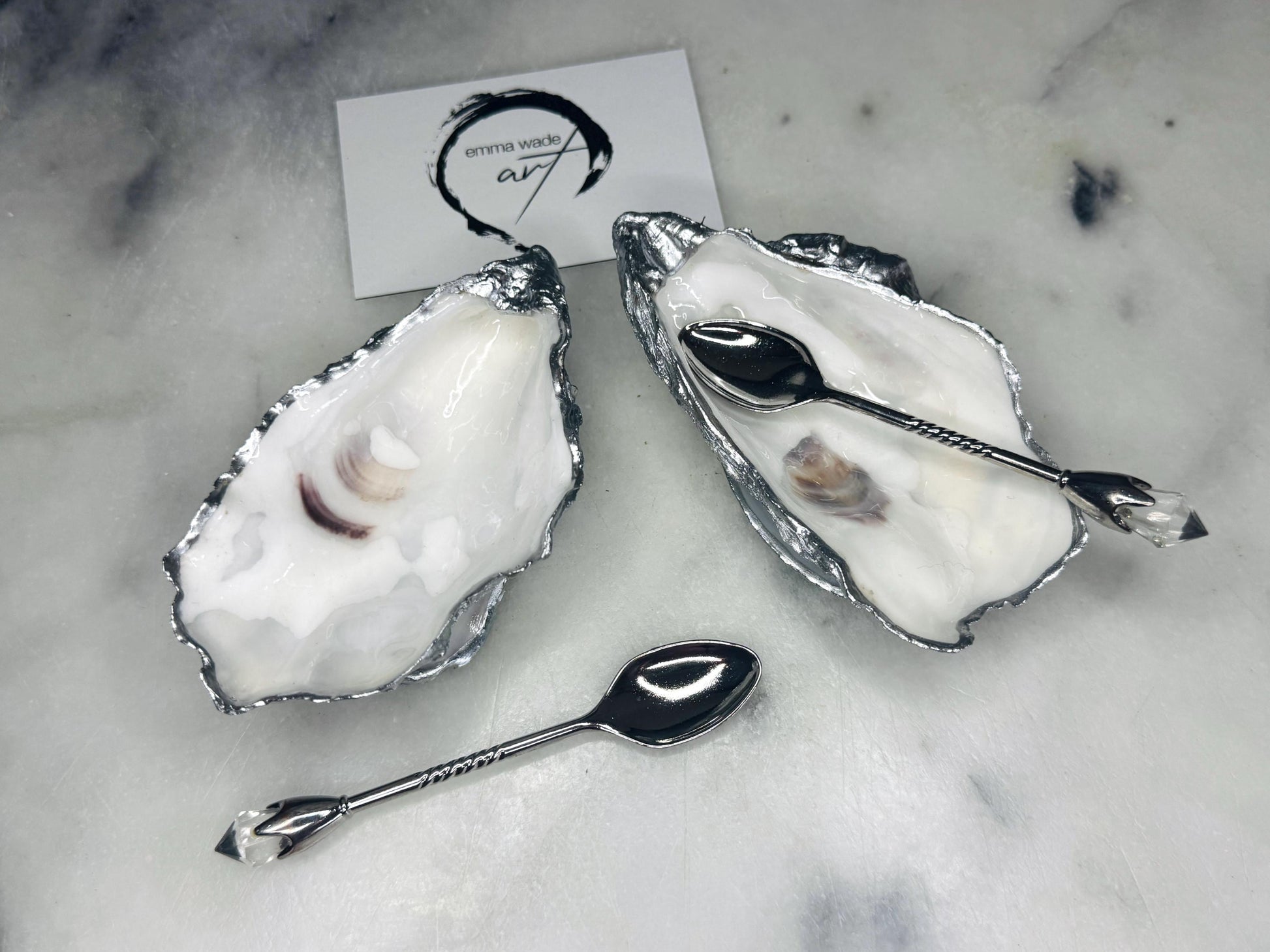 Handmade pearl oyster shell salt and pepper pinch pots with silver leaf accents and optional crystal spoons. Coastal tableware set made from natural Dorset oyster shells, polished to a natural white pearl finish and sealed with food-safe glossy resin. Elegant shell salt dishes photographed on a light background, showing two domed shells with matching bases, ideal for serving salt, pepper or spices at stylish dinner tables and special occasions.
