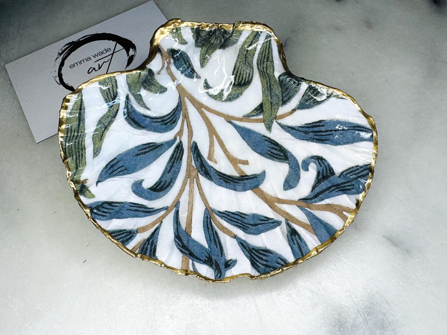 Handmade Dorset scallop shell trinket dish featuring William Morris Willow Bough design in soft blue and green tones. Decorative shell jewellery dish finished with hand-applied liquid gold leaf edging and glossy resin. Coastal inspired ring holder with botanical Arts and Crafts pattern and natural shell shape, styled as elegant bathroom décor and heritage home accessory.