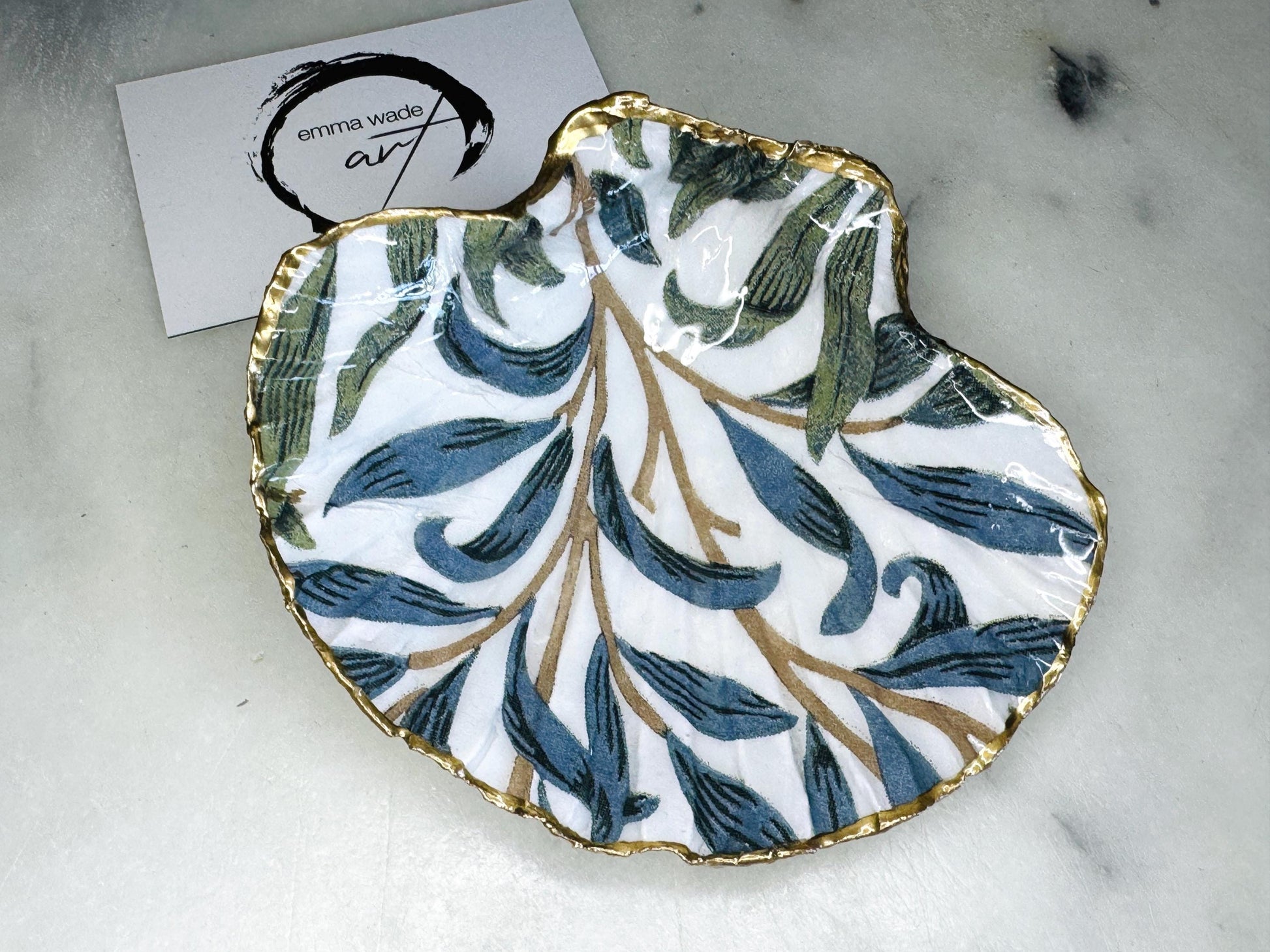 Handmade Dorset scallop shell trinket dish featuring William Morris Willow Bough design in soft blue and green tones. Decorative shell jewellery dish finished with hand-applied liquid gold leaf edging and glossy resin. Coastal inspired ring holder with botanical Arts and Crafts pattern and natural shell shape, styled as elegant bathroom décor and heritage home accessory.