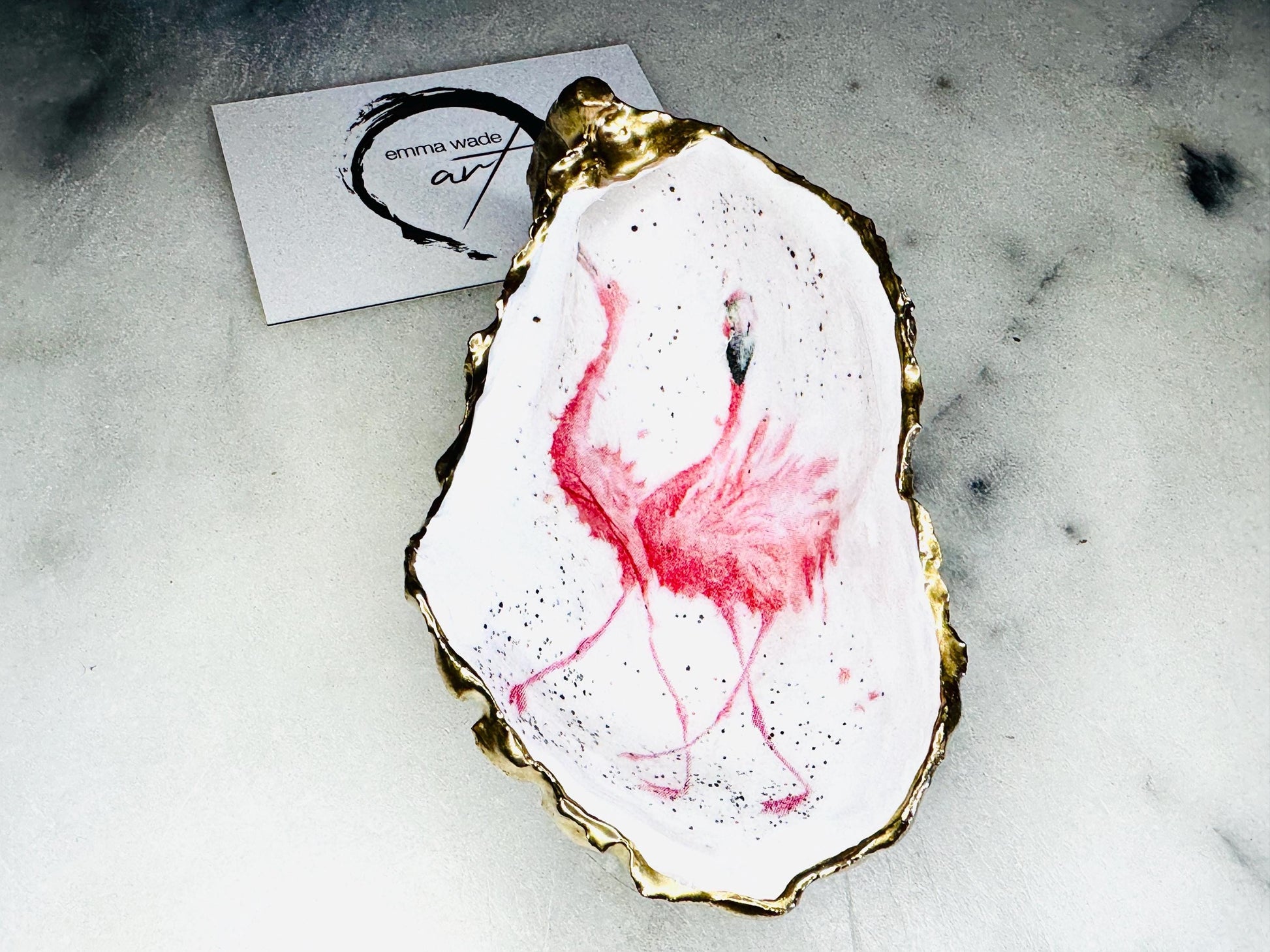 Handmade Dorset oyster shell trinket dishes featuring elegant pink flamingo bird artwork with hand-painted gold leaf edging and glossy crystal clear resin. Coastal flamingo jewellery holders styled on a white marble background with tropical blush pink tones and luxury coastal home décor styling.