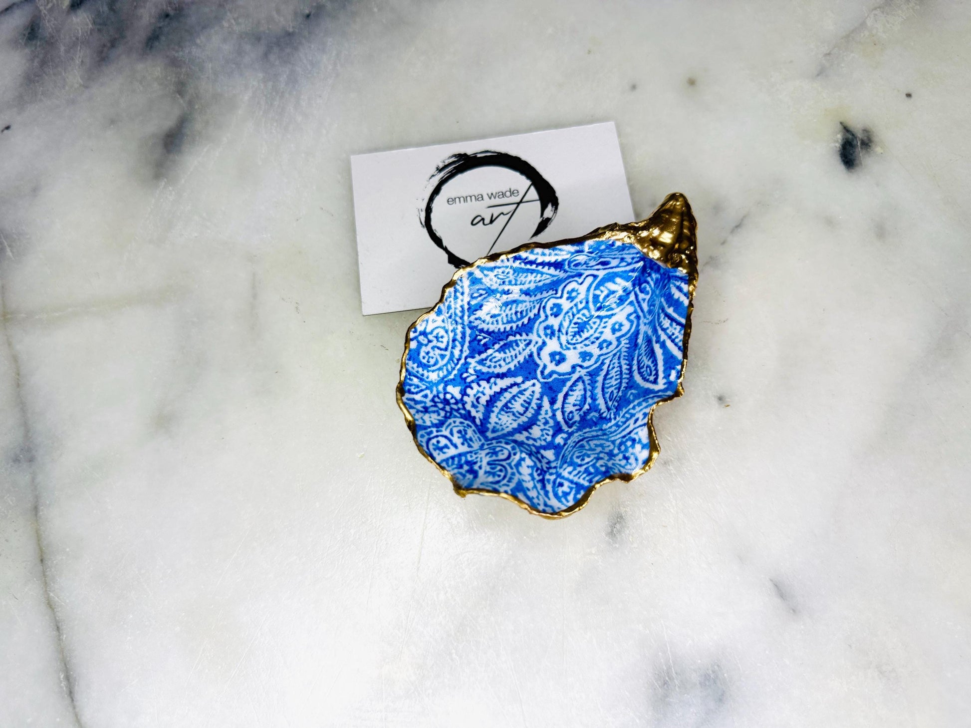 Handmade Dorset oyster shell trinket dish featuring an elegant blue and white paisley design, hand-gilded with liquid gold leaf and finished in glossy resin. Coastal shell jewellery holder available in multiple sizes from small to XL, ideal as a ring dish, trinket tray, vanity decor, or luxury coastal gift.