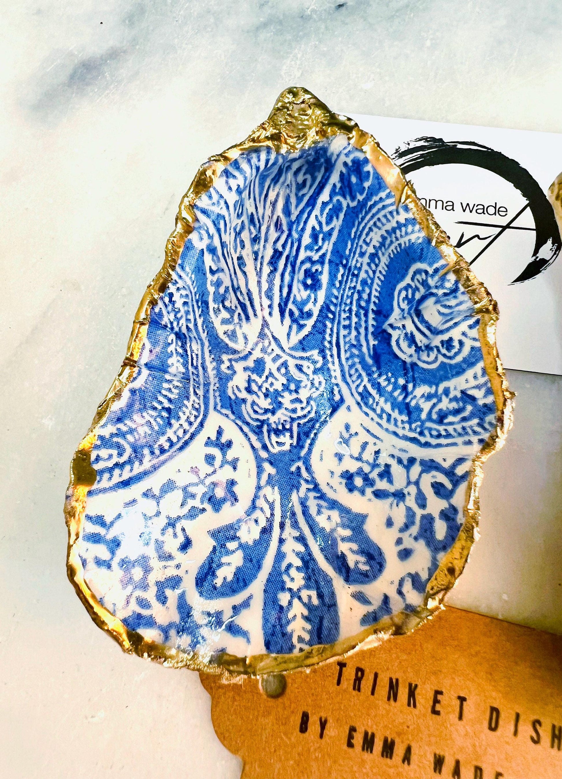 Handmade Dorset oyster shell trinket dish featuring an elegant blue and white paisley design, hand-gilded with liquid gold leaf and finished in glossy resin. Coastal shell jewellery holder available in multiple sizes from small to XL, ideal as a ring dish, trinket tray, vanity decor, or luxury coastal gift.