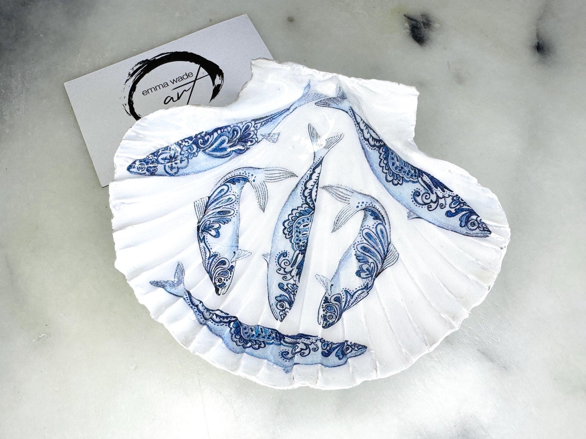 Handmade Dorset scallop shell trinket dishes featuring blue and white paisley fish illustrations with hand-painted gold leaf edging and glossy crystal clear resin. Coastal Scandinavian inspired jewellery dishes styled on a soft neutral background with elegant nautical fish artwork and luxurious gilded detailing.