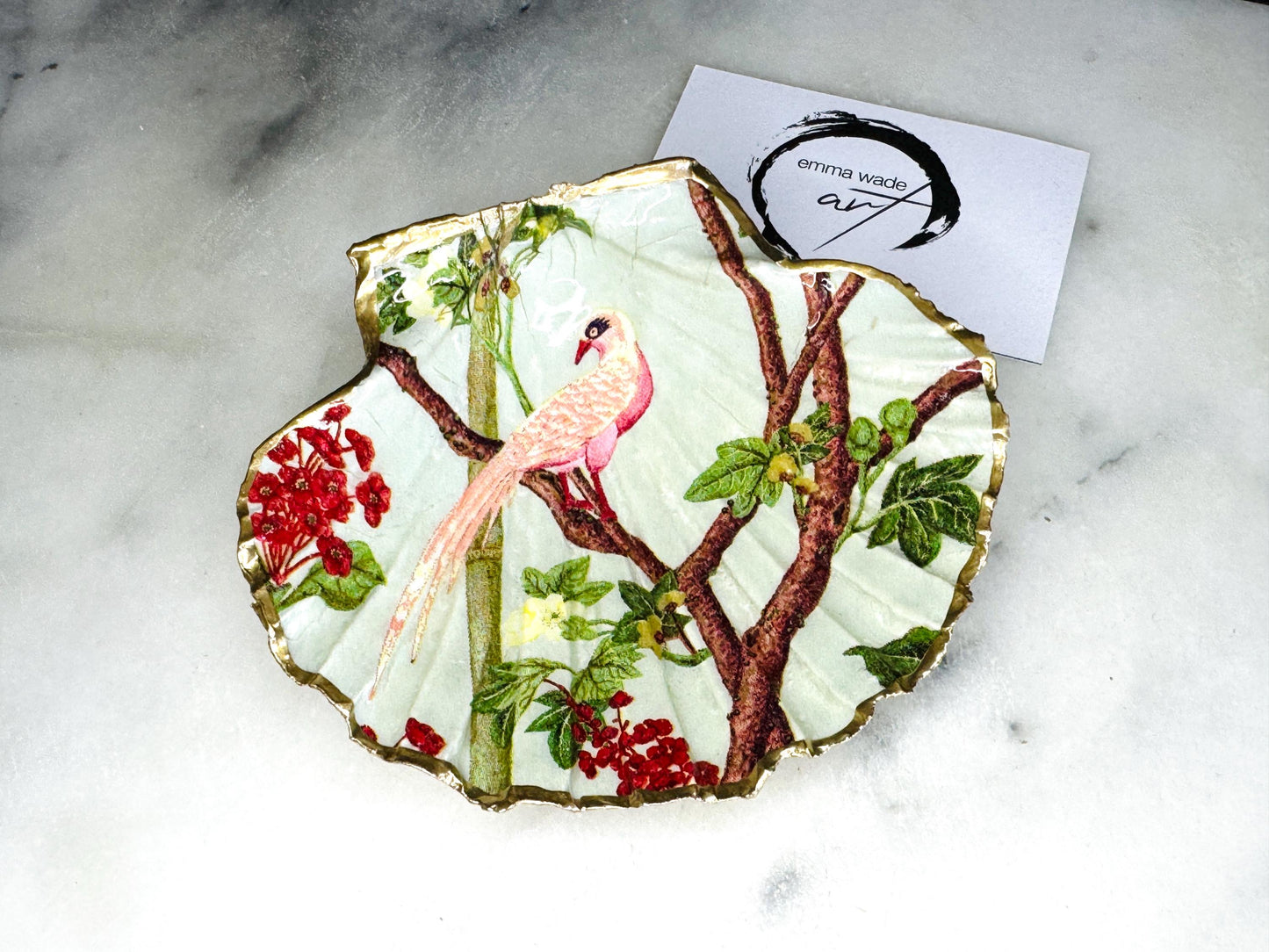 Handmade Dorset scallop shell trinket dish featuring delicate pink bird and botanical branch design with hand gilded gold leaf edging and glossy resin finish, elegant coastal jewellery holder inspired by birds of paradise and nature