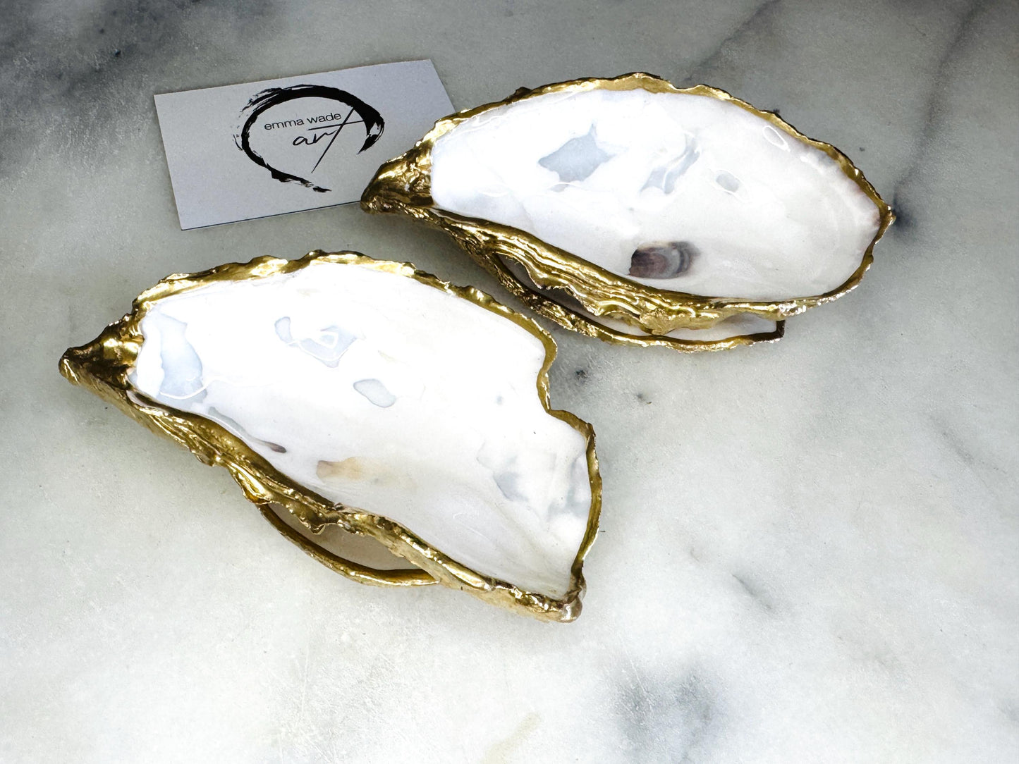 Handmade gold leaf oyster shell salt cellar set with pearl interiors and matching spoons. Coastal pinch pots made from Dorset oyster shells, sealed with glossy resin and finished with gilded edges. Luxury tableware set photographed on a light background, showing two shell salt dishes and decorative spoons as add ons, perfect for serving salt or spices at the table.