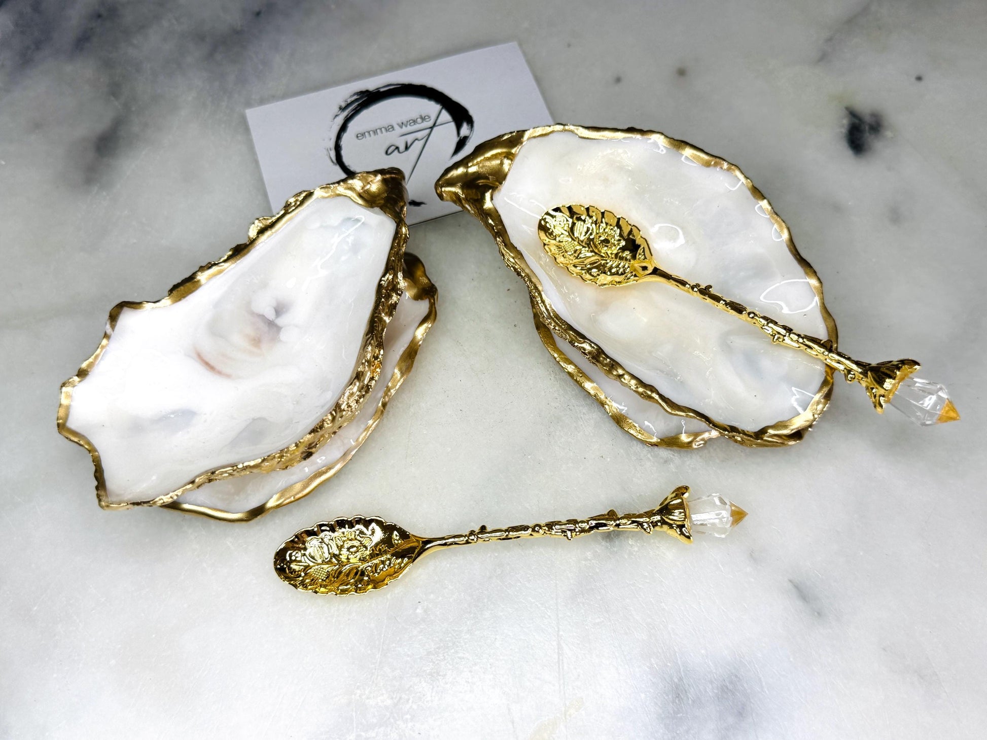 Handmade gold leaf oyster shell salt cellar set with pearl interiors and matching spoons. Coastal pinch pots made from Dorset oyster shells, sealed with glossy resin and finished with gilded edges. Luxury tableware set photographed on a light background, showing two shell salt dishes and decorative spoons, perfect for serving salt or spices at the table.