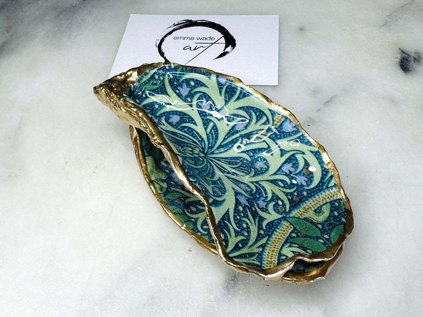 William Morris Seaweed design decoupage oyster shell ring dish with gold leaf exterior and glossy resin finish, shown on a light background. Natural Dorset oyster shell jewellery dish used as a ring holder, featuring a green and blue patterned interior, polished edges, and handcrafted coastal keepsake style. Ideal as an engagement ring dish, wedding ring holder, or jewellery trinket dish.