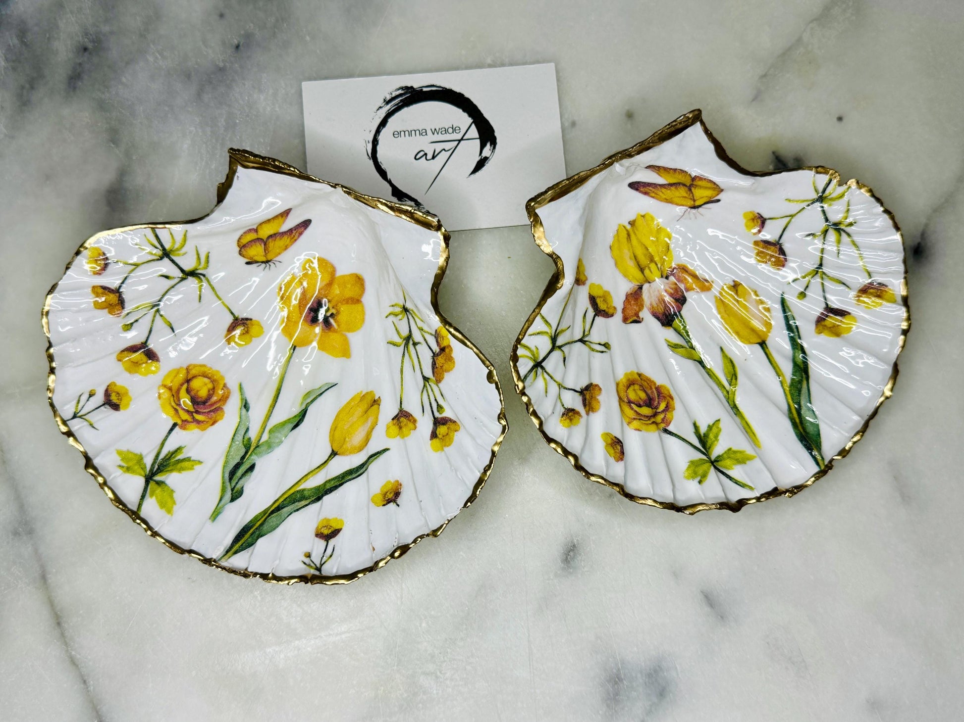 Hand finished scallop shell trinket dish featuring yellow spring flower artwork with a hand gilded gold leaf rim, sealed in glossy clear resin for durability and shine. Coastal inspired shell jewellery dish photographed on a light surface, ideal for rings, earrings and small keepsakes. Decorative floral shell dish by EmmaWadeART inspired by the Dorset coastline, perfect as a gift or elegant home décor accent.