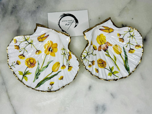 Hand finished scallop shell trinket dish featuring yellow spring flower artwork with a hand gilded gold leaf rim, sealed in glossy clear resin for durability and shine. Coastal inspired shell jewellery dish photographed on a light surface, ideal for rings, earrings and small keepsakes. Decorative floral shell dish by EmmaWadeART inspired by the Dorset coastline, perfect as a gift or elegant home décor accent.