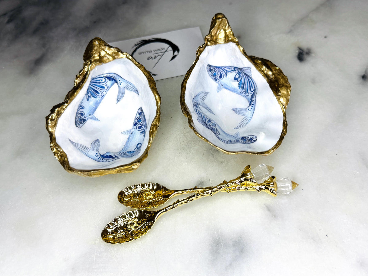 Handmade Dorset oyster shell salt and pepper pinch pots featuring blue paisley fish designs with gold leaf edging and glossy resin finish. Coastal oyster shell cruet set with natural pearlescent interiors and optional gold spoons, styled as elegant nautical table décor and condiment dishes.