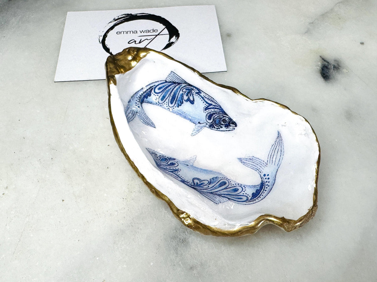 Handmade Dorset oyster shell trinket dish with blue and white paisley fish design, gold leaf gilded edges and glossy resin finish. Coastal jewellery holder and ring dish, photographed on a light surface showing the natural shell shape and pearly interior. Unique sustainably sourced shell, sold individually as a decorative coastal home décor accent or gift.