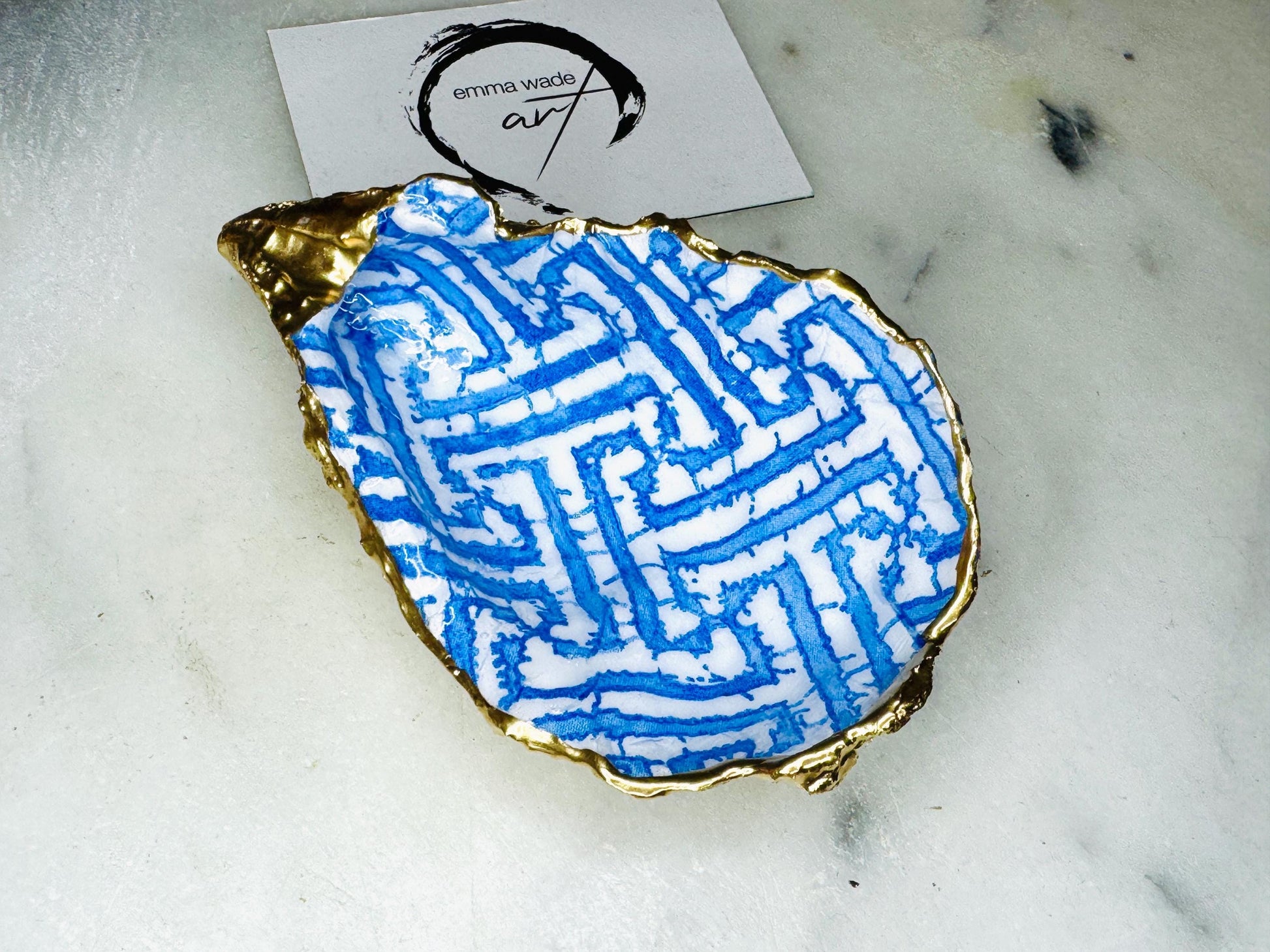 Handmade blue fretwork oyster shell trinket dish shown as a single piece, crafted from a natural Dorset oyster shell and finished with genuine gold leaf edges and glossy resin. Featuring an intricate blue fretwork pattern, this jewellery and ring holder is perfect for a bedside table, bathroom or coastal-inspired decor. Each shell is one of a kind and carefully finished by hand.