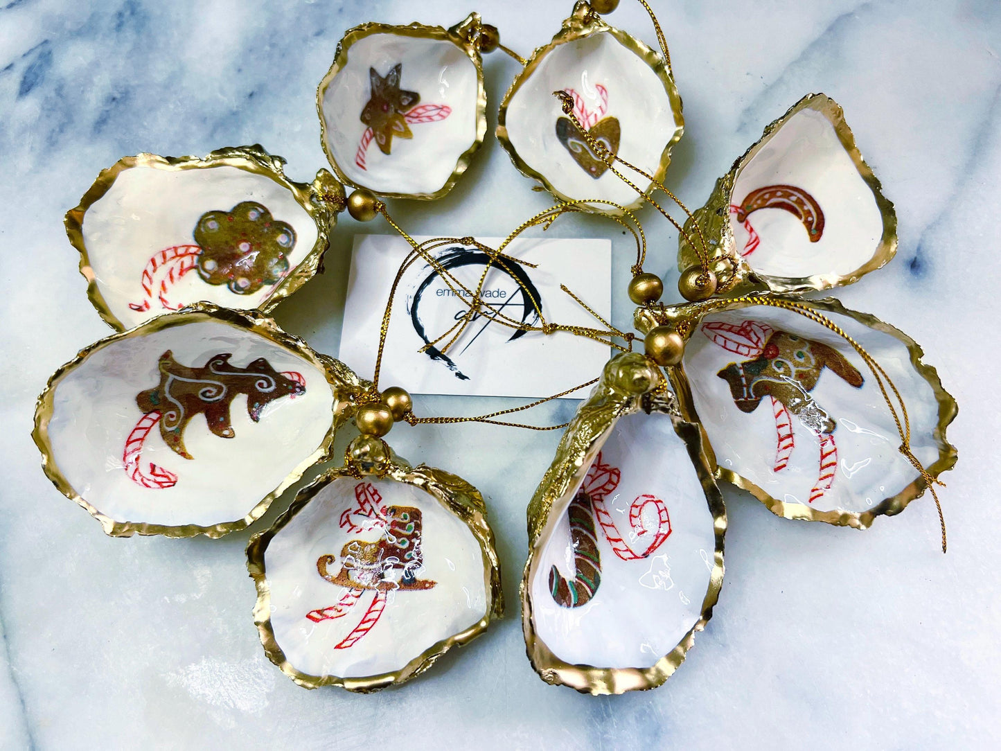 Handcrafted Dorset oyster shell Christmas ornaments featuring gingerbread-inspired festive motifs including candy canes, stars, moons, hearts, and skates. Gold leaf edged coastal Christmas baubles with glossy resin finish and pearl shell interiors displayed as luxury handmade holiday decorations.