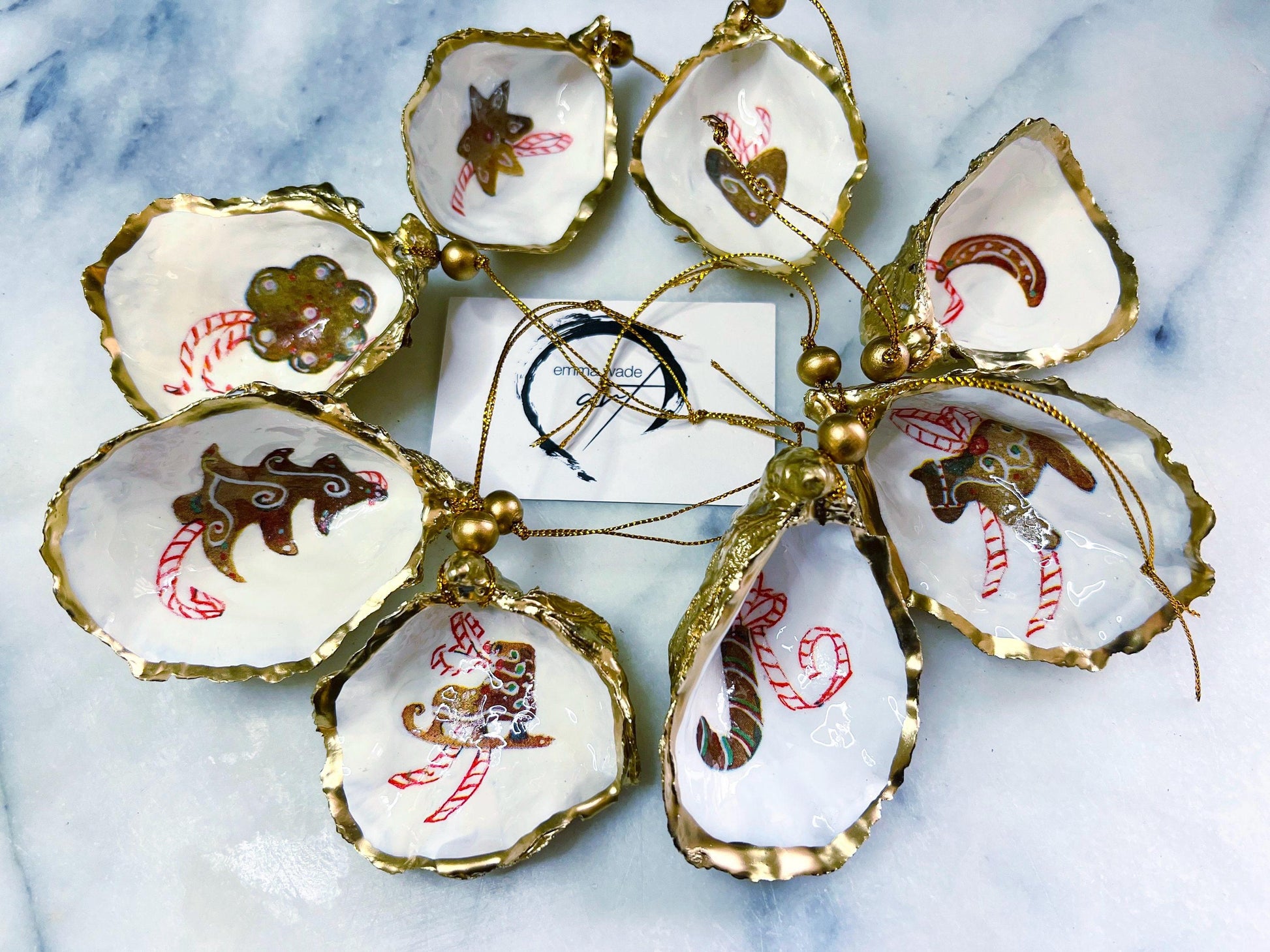 Handcrafted Dorset oyster shell Christmas ornaments featuring gingerbread-inspired festive motifs including candy canes, stars, moons, hearts, and skates. Gold leaf edged coastal Christmas baubles with glossy resin finish and pearl shell interiors displayed as luxury handmade holiday decorations.