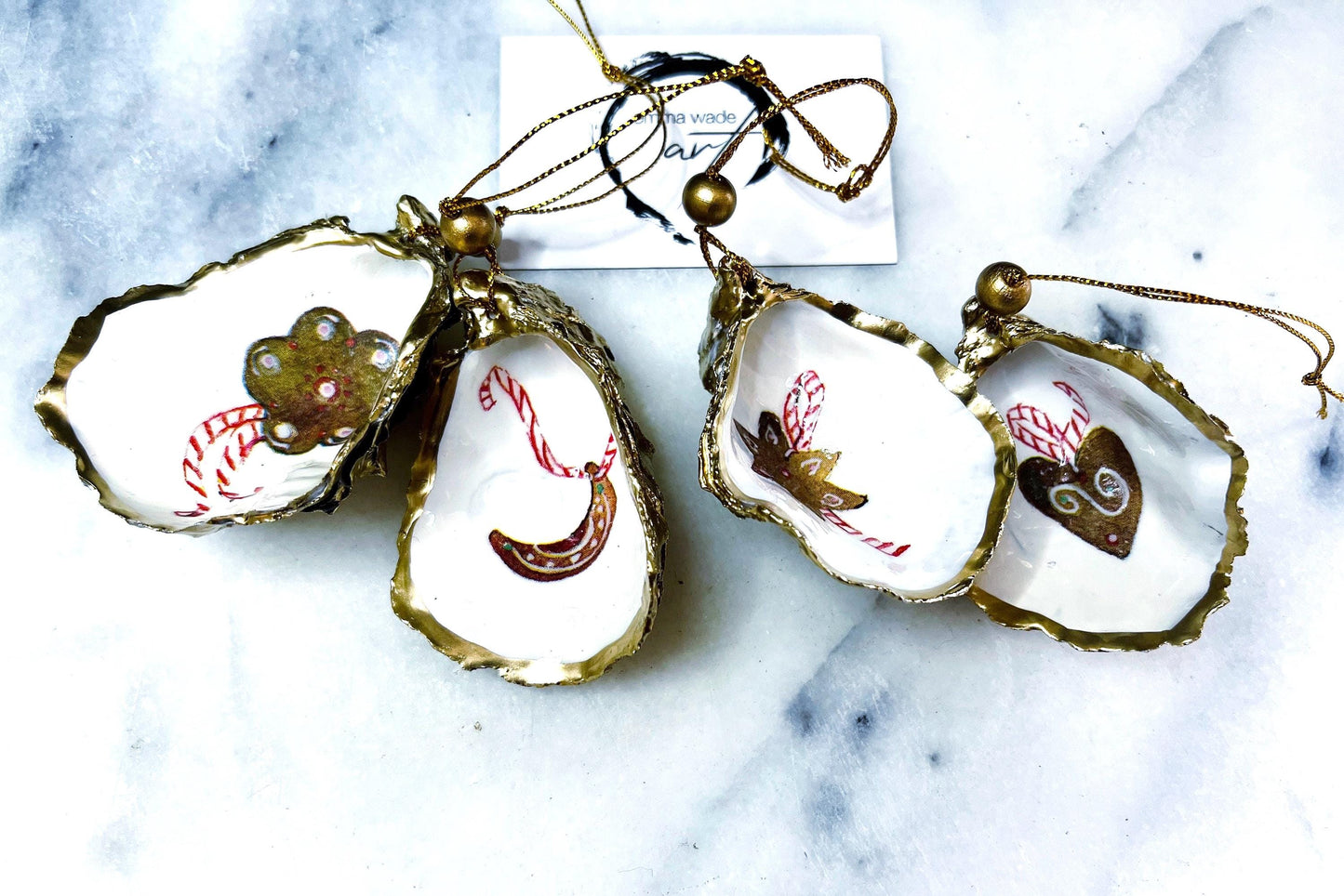 Handcrafted Dorset oyster shell Christmas ornaments featuring gingerbread-inspired festive motifs including candy canes, stars, moons, hearts, and skates. Gold leaf edged coastal Christmas baubles with glossy resin finish and pearl shell interiors displayed as luxury handmade holiday decorations.