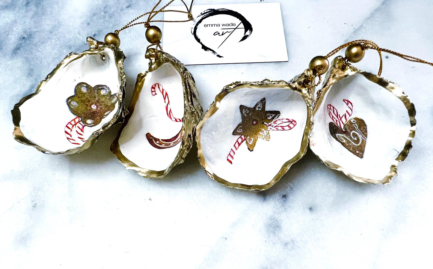Handcrafted Dorset oyster shell Christmas ornaments featuring gingerbread-inspired festive motifs including candy canes, stars, moons, hearts, and skates. Gold leaf edged coastal Christmas baubles with glossy resin finish and pearl shell interiors displayed as luxury handmade holiday decorations.