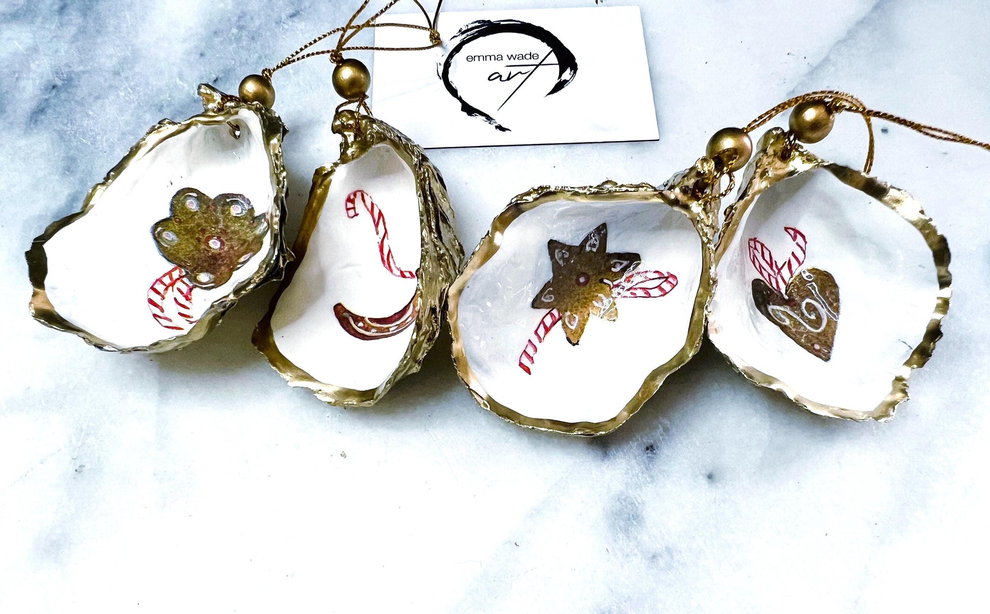 Handcrafted Dorset oyster shell Christmas ornaments featuring gingerbread-inspired festive motifs including candy canes, stars, moons, hearts, and skates. Gold leaf edged coastal Christmas baubles with glossy resin finish and pearl shell interiors displayed as luxury handmade holiday decorations.