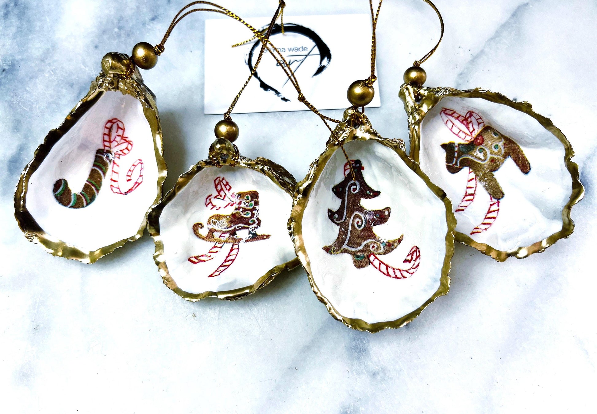 Handcrafted Dorset oyster shell Christmas ornaments featuring gingerbread-inspired festive motifs including candy canes, stars, moons, hearts, and skates. Gold leaf edged coastal Christmas baubles with glossy resin finish and pearl shell interiors displayed as luxury handmade holiday decorations.