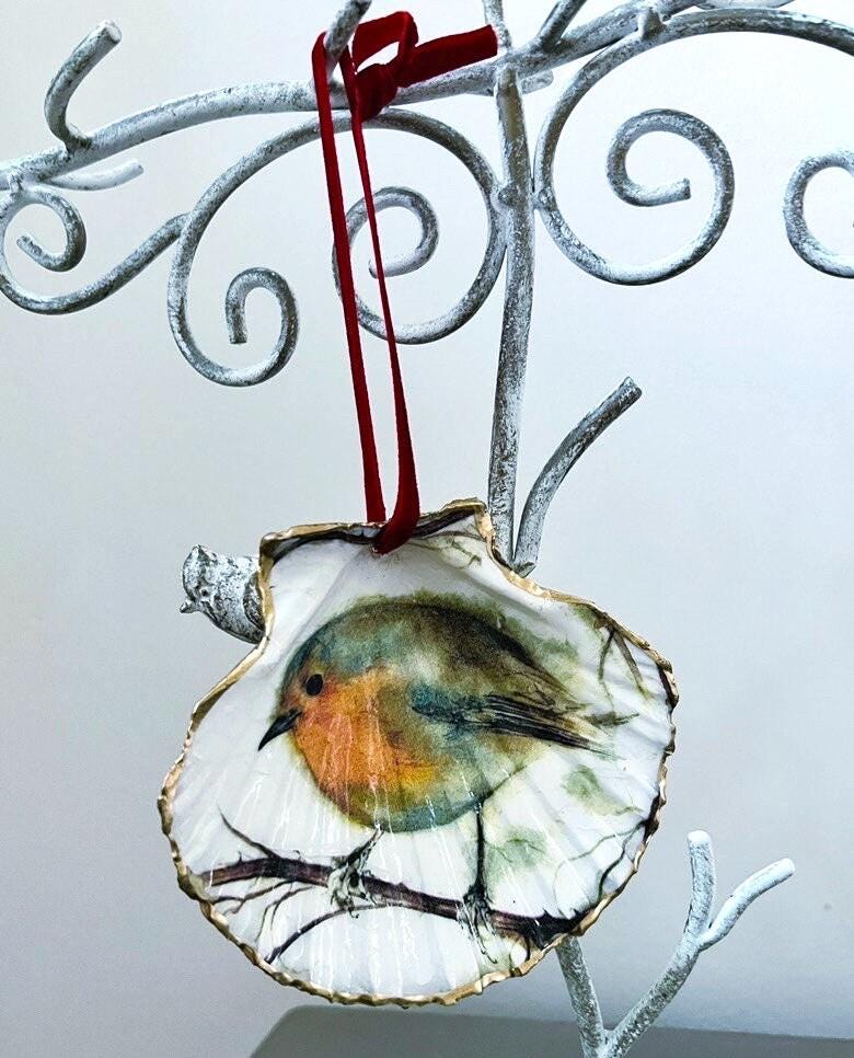 Handcrafted Dorset scallop shell trinket dish featuring a robin redbreast illustration with gold leaf edging and glossy resin finish. Coastal cottagecore jewellery holder and Christmas hanging ornament with natural shell texture and festive British bird design.