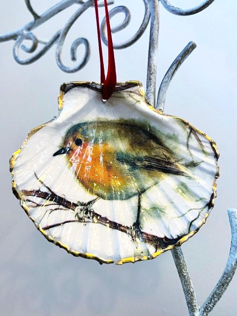 Handcrafted Dorset scallop shell trinket dish featuring a robin redbreast illustration with gold leaf edging and glossy resin finish. Coastal cottagecore jewellery holder and Christmas hanging ornament with natural shell texture and festive British bird design.