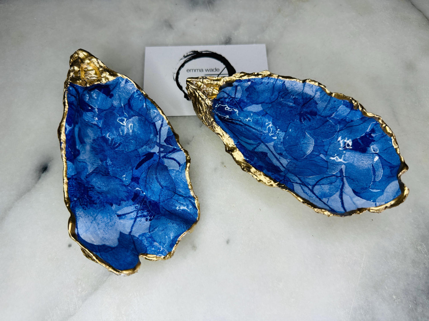 Pair of oyster shell salt and pepper dishes with deep blue watercolour flower design, finished with gold leaf trim and glossy seal. Handmade from Dorset oyster shells, each dish is unique with natural variations. A beautiful oyster shell salt gift set, also available with matching gold crystal spoons for a finishing touch. Perfect for weddings, anniversaries, dinner parties, or as a handmade gift for birthdays, Christmas, or housewarmings. Elegant coastal tableware and decor piece.