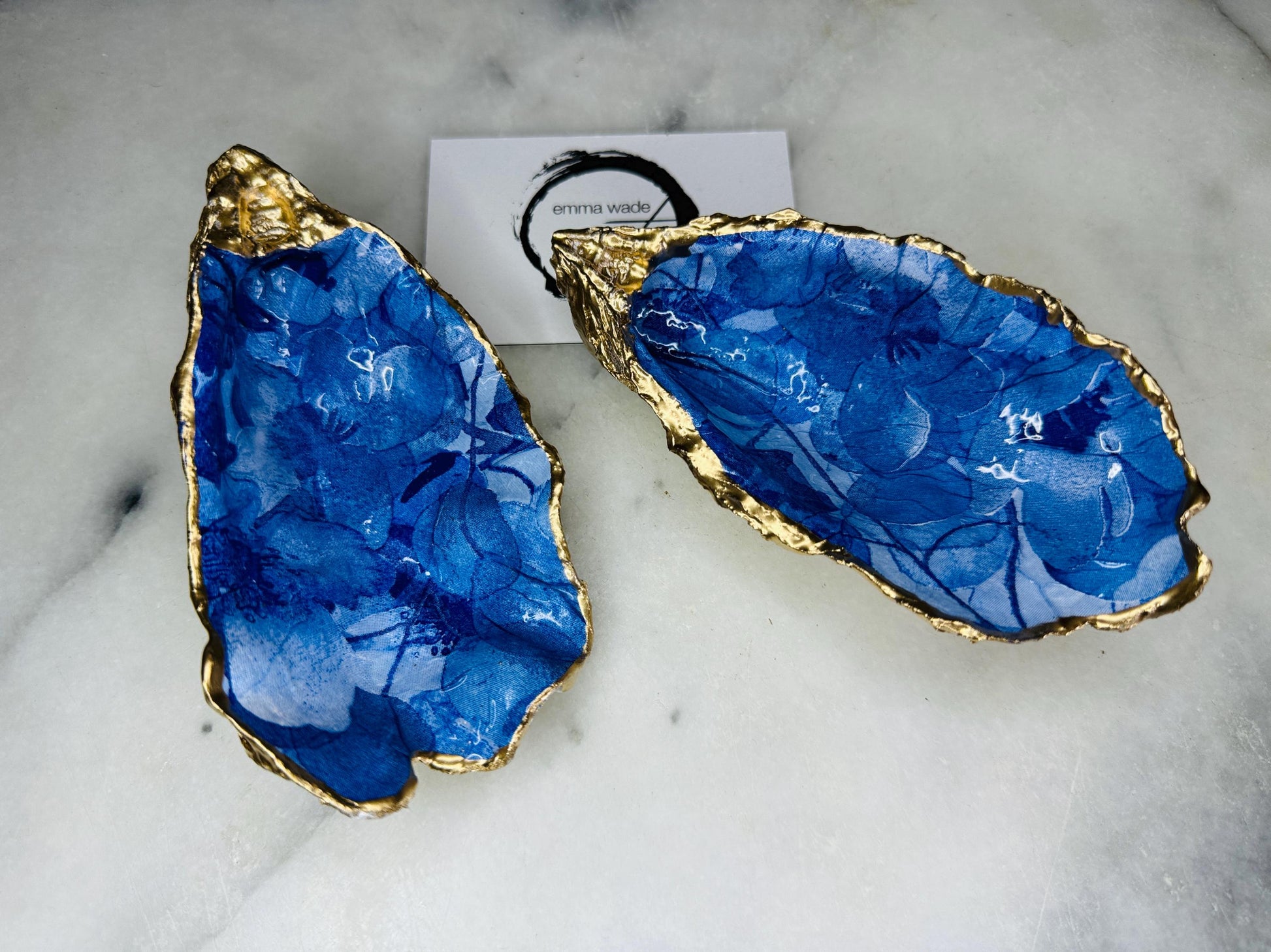 Pair of oyster shell salt and pepper dishes with deep blue watercolour flower design, finished with gold leaf trim and glossy seal. Handmade from Dorset oyster shells, each dish is unique with natural variations. A beautiful oyster shell salt gift set, also available with matching gold crystal spoons for a finishing touch. Perfect for weddings, anniversaries, dinner parties, or as a handmade gift for birthdays, Christmas, or housewarmings. Elegant coastal tableware and decor piece.