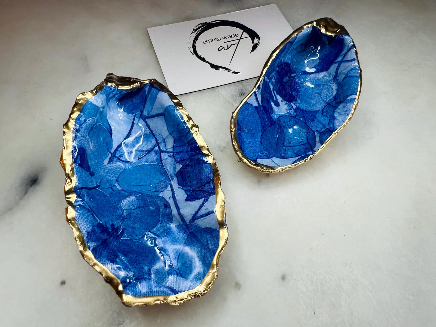 Pair of oyster shell salt and pepper dishes with deep blue watercolour flower design, finished with gold leaf trim and glossy seal. Handmade from Dorset oyster shells, each dish is unique with natural variations. A beautiful oyster shell salt gift set, also available with matching gold crystal spoons for a finishing touch. Perfect for weddings, anniversaries, dinner parties, or as a handmade gift for birthdays, Christmas, or housewarmings. Elegant coastal tableware and decor piece.