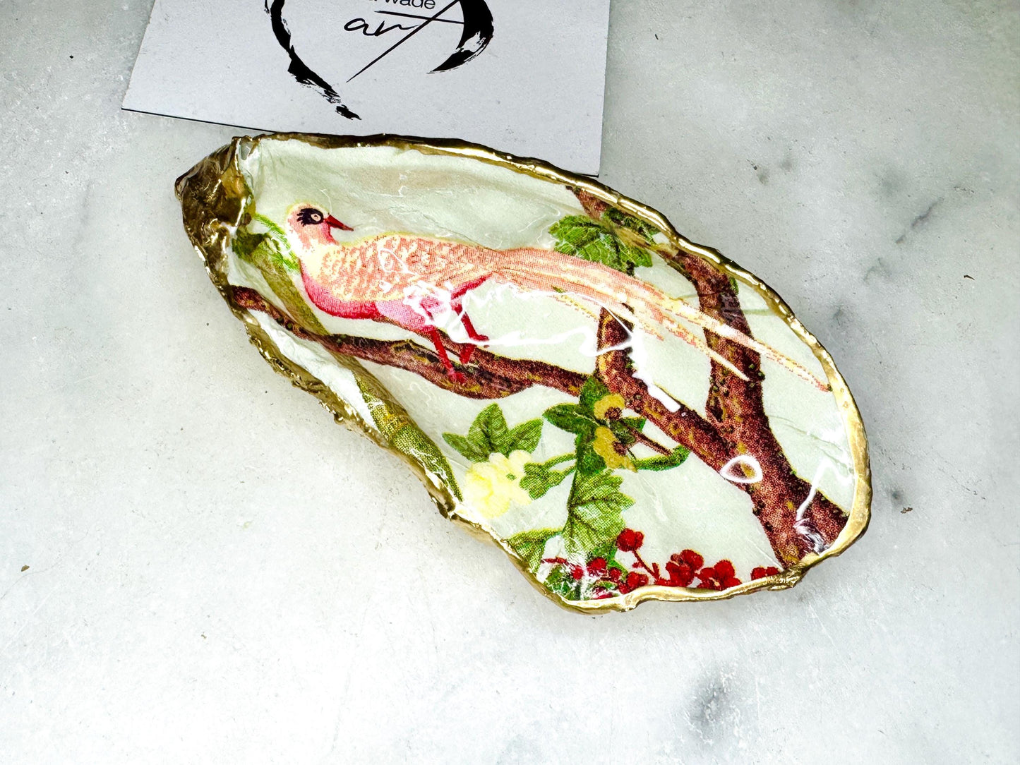 Handmade oyster shell trinket dish featuring colourful Bird of Paradise artwork with gold leaf edging and glossy resin finish. Tropical coastal jewellery dish crafted from natural Dorset shells, styled as a ring holder, keepsake tray, or exotic nature-inspired gift.