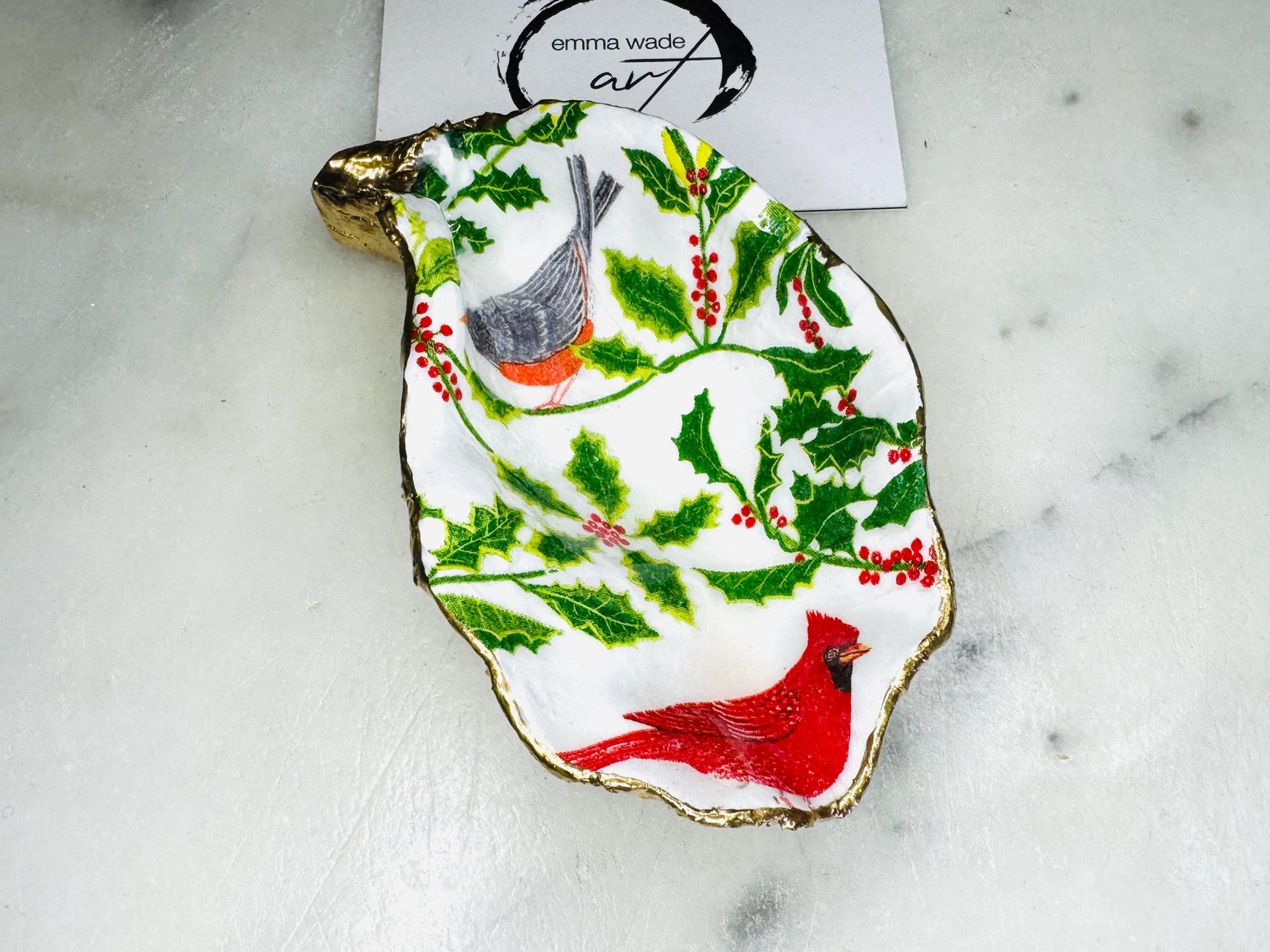 Handmade Dorset oyster shell Christmas ornament featuring red and orange winter birds perched amongst festive green foliage and berries. Coastal oyster shell trinket dish with hand applied gold leaf edging and glossy resin finish, styled as luxury Christmas décor. Sustainable handcrafted robin-inspired shell decoration available as hanging ornament or jewellery dish, inspired by British winter wildlife and the Dorset coastline.