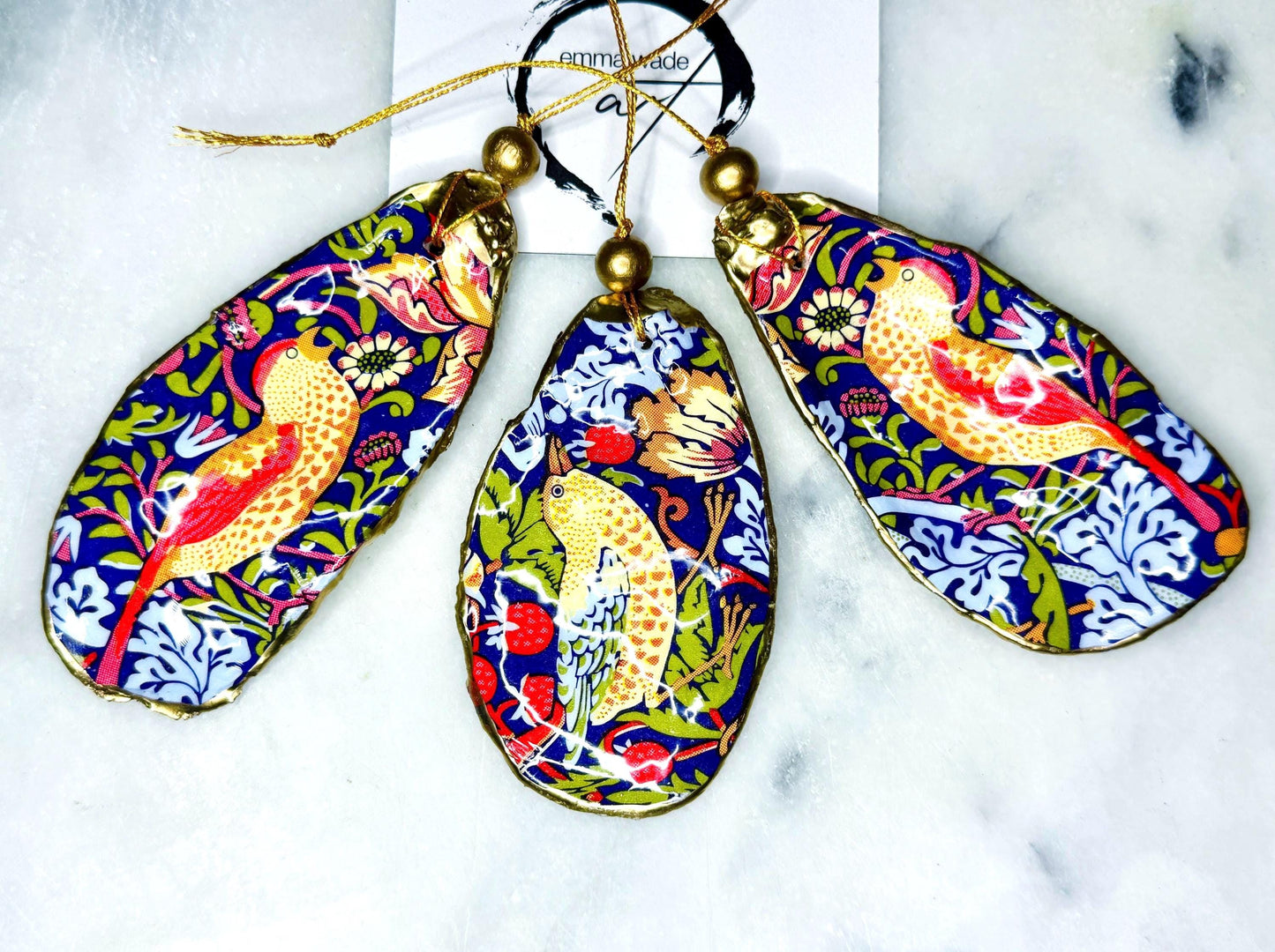 William Morris Strawberry Thief oyster shell ornaments with gold leaf edging, handcrafted from Dorset flat oyster shells and finished in glossy resin. Luxury hanging Christmas decorations featuring the iconic red Strawberry Thief bird motif with polished pearl interiors, gold hanging cords and artisan coastal styling. Available individually or as matching ornament sets for Christmas trees, gifting, weddings and home décor.
