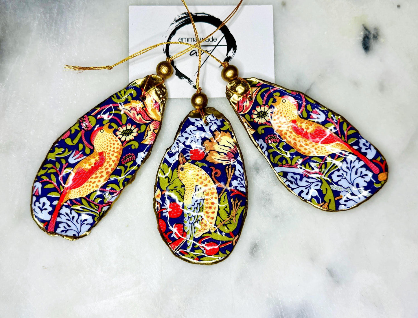 William Morris Strawberry Thief oyster shell ornaments with gold leaf edging, handcrafted from Dorset flat oyster shells and finished in glossy resin. Luxury hanging Christmas decorations featuring the iconic red Strawberry Thief bird motif with polished pearl interiors, gold hanging cords and artisan coastal styling. Available individually or as matching ornament sets for Christmas trees, gifting, weddings and home décor.