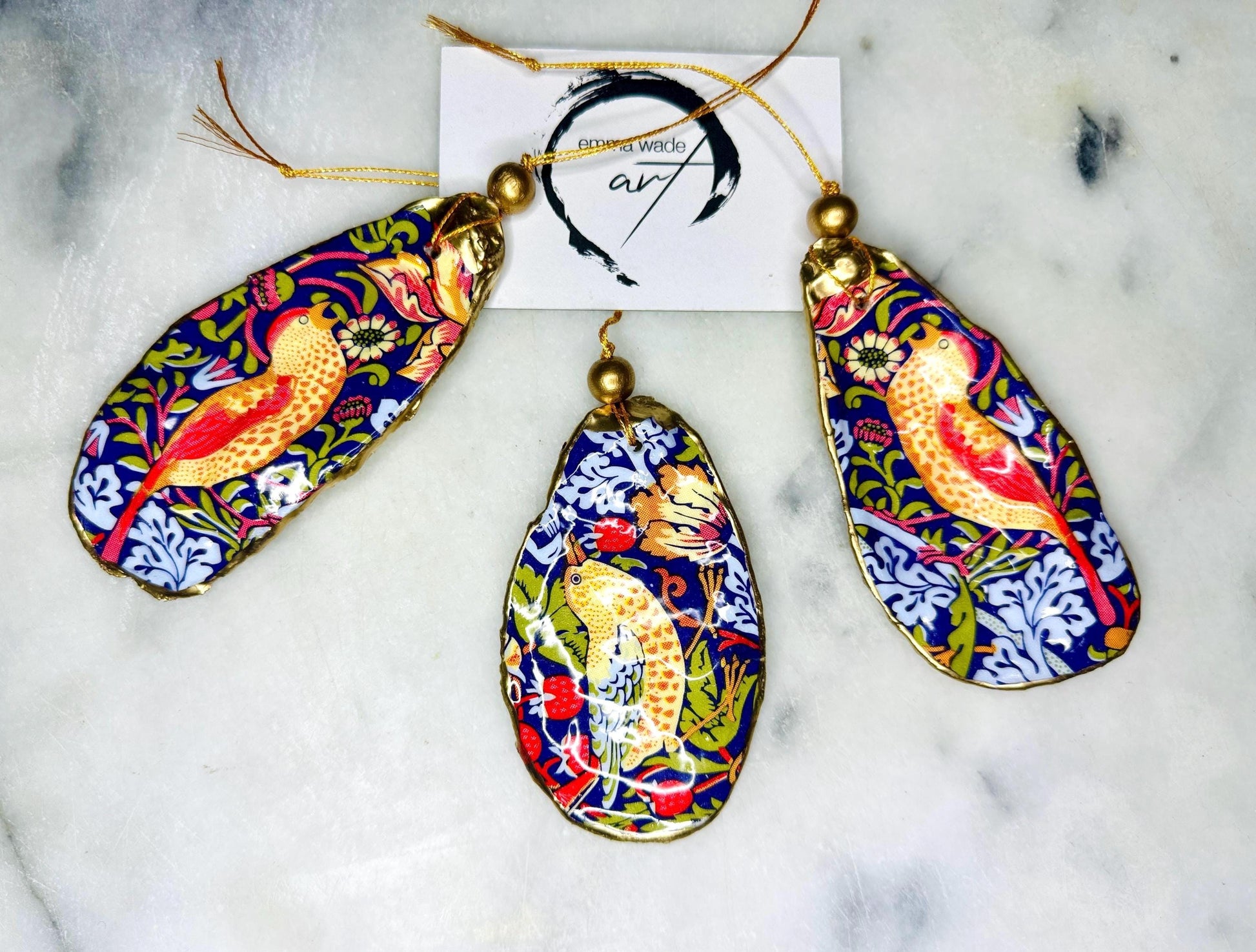 William Morris Strawberry Thief oyster shell ornaments with gold leaf edging, handcrafted from Dorset flat oyster shells and finished in glossy resin. Luxury hanging Christmas decorations featuring the iconic red Strawberry Thief bird motif with polished pearl interiors, gold hanging cords and artisan coastal styling. Available individually or as matching ornament sets for Christmas trees, gifting, weddings and home décor.