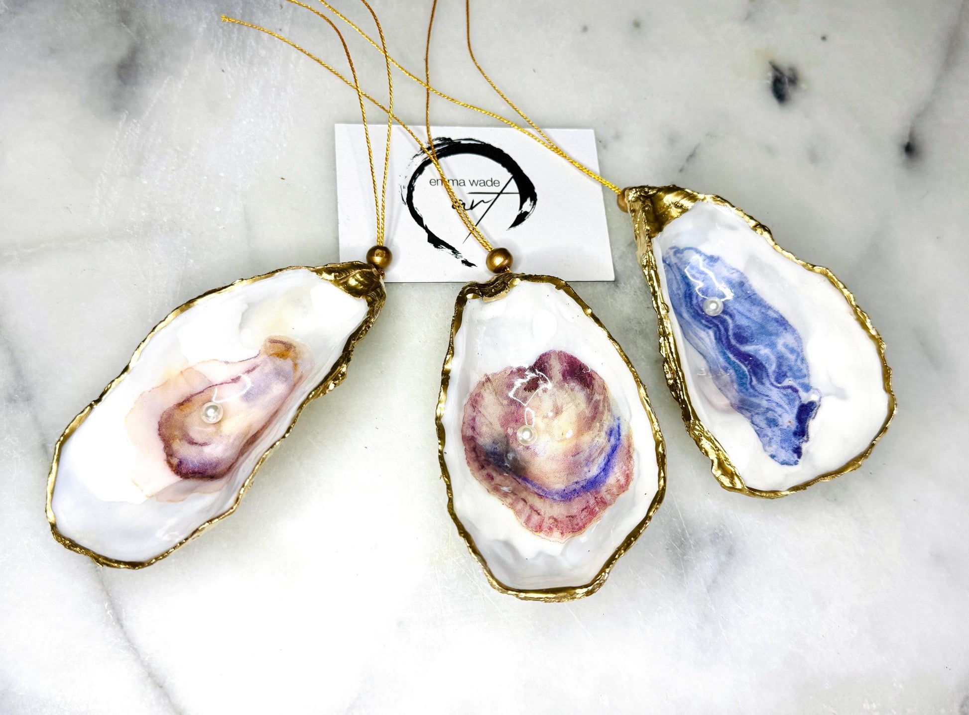 Handcrafted Dorset oyster shell hanging ornament decorated with a Swarovski pearl. Each natural oyster shell is finished with liquid gold leaf on the rim and back, sealed with crystal-clear glossy resin, and strung with gold cord and bead. Unique coastal Christmas decoration or tree bauble that can also be displayed year-round. A beautiful handmade oyster shell gift, ideal for weddings, anniversaries, Christmas stockings, bridesmaid keepsakes, or coastal-inspired home décor.