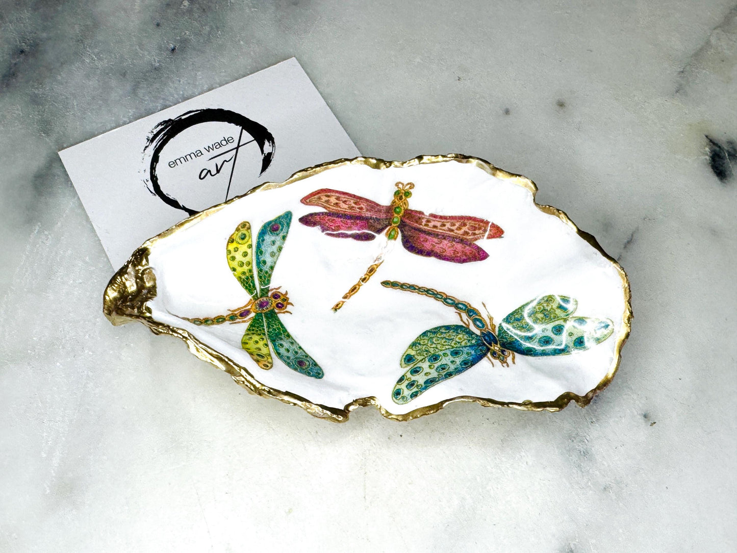 Handmade dragonfly oyster shell trinket dish with hand-gilded gold leaf edges and glossy resin finish, created from sustainably sourced Dorset shells. Unique coastal jewellery holder and ring dish, ideal as a vanity tray, trinket tray or decorative keepsake. Nature inspired home decor gift for birthdays, weddings, anniversaries, housewarmings and Mother’s Day. One of a kind artisan shell dish, beautifully presented in a gift box.