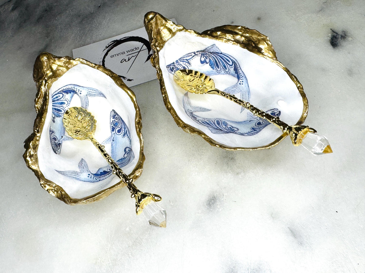 Handmade Dorset oyster shell salt and pepper pinch pots featuring blue paisley fish designs with gold leaf edging and glossy resin finish. Coastal oyster shell cruet set with natural pearlescent interiors and optional gold spoons, styled as elegant nautical table décor and condiment dishes.