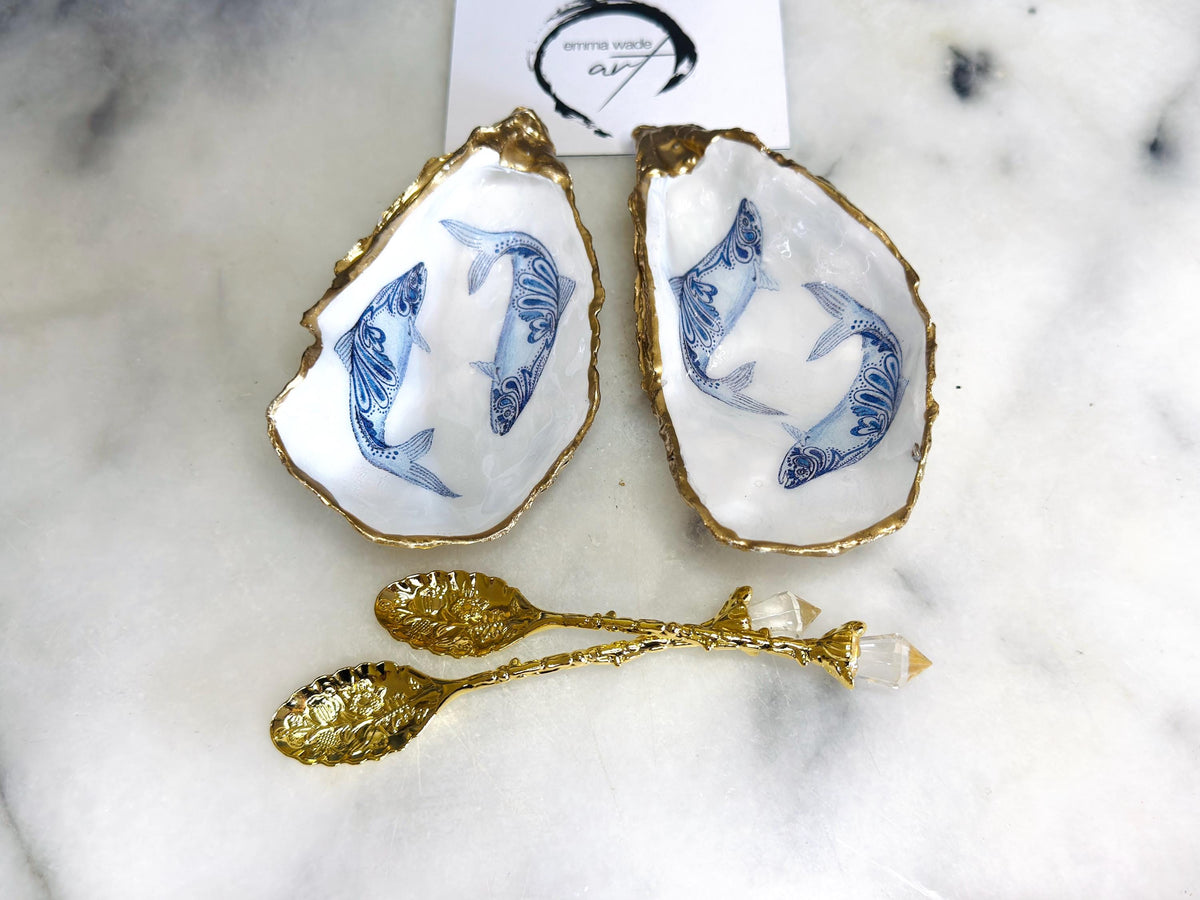 Handmade Dorset oyster shell salt and pepper pinch pots featuring blue paisley fish designs with gold leaf edging and glossy resin finish. Coastal oyster shell cruet set with natural pearlescent interiors and optional gold spoons, styled as elegant nautical table décor and condiment dishes.