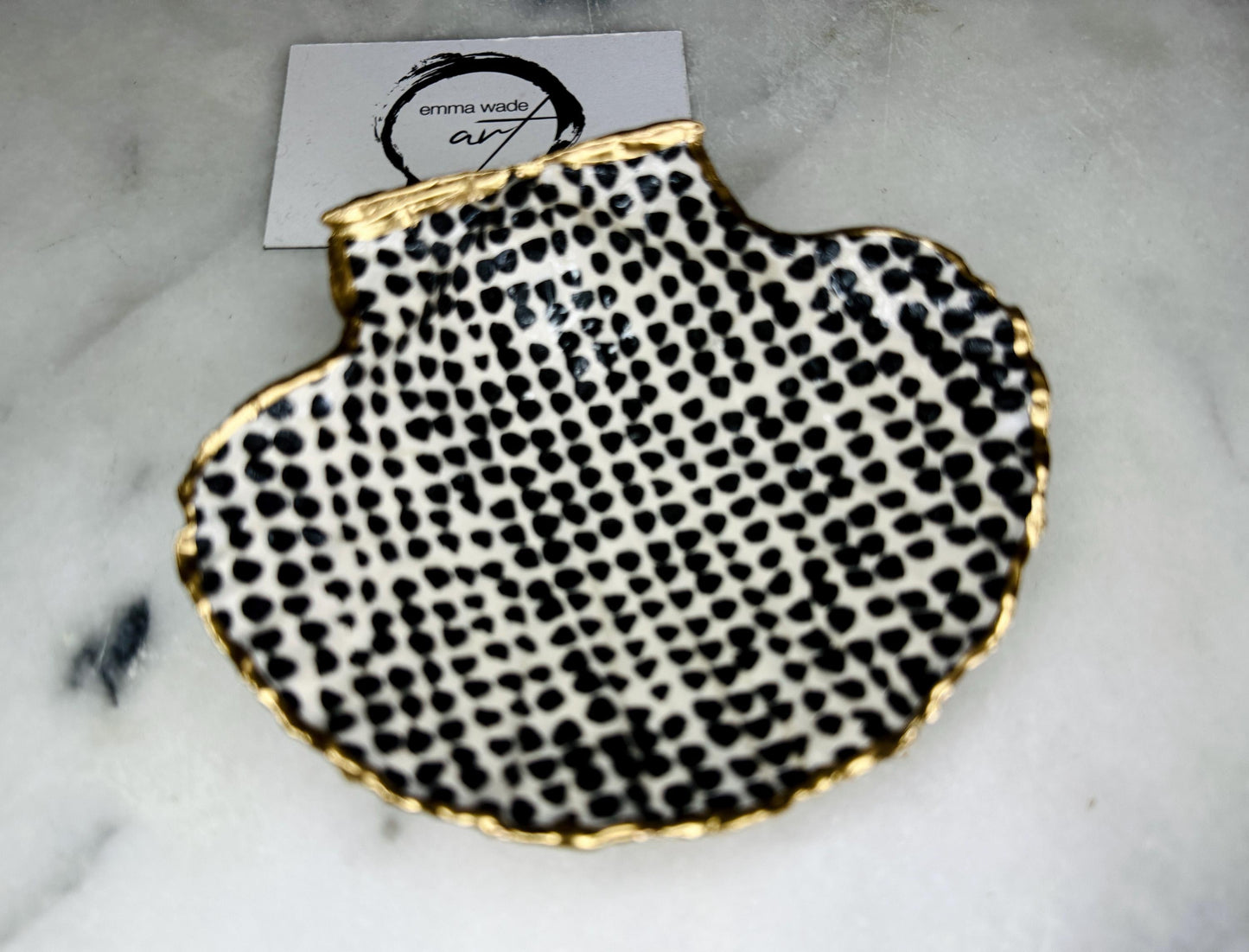 Handcrafted black and white dotted Dorset scallop shell trinket dish, gilded with real gold leaf and sealed in crystal-clear resin. Perfect as a jewellery holder, cufflink tray, tea light holder, or coastal home accent. Each eco-friendly shell is ethically sourced from the Dorset coastline, individually hand finished in Surrey, and presented in a sustainable gift box. A thoughtful handmade gift for ocean lovers, weddings, birthdays, or coastal home décor.