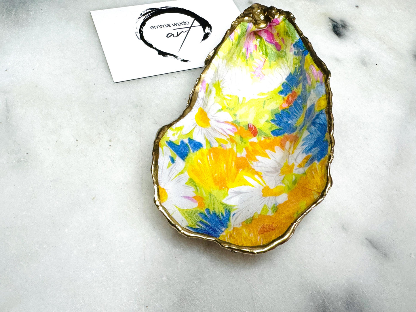 Handmade Dorset oyster shell trinket dish featuring colourful floral artwork in pink, yellow, orange, and blue tones with genuine gold leaf edging and glossy resin finish. Coastal jewellery holder and vibrant floral home décor gift.