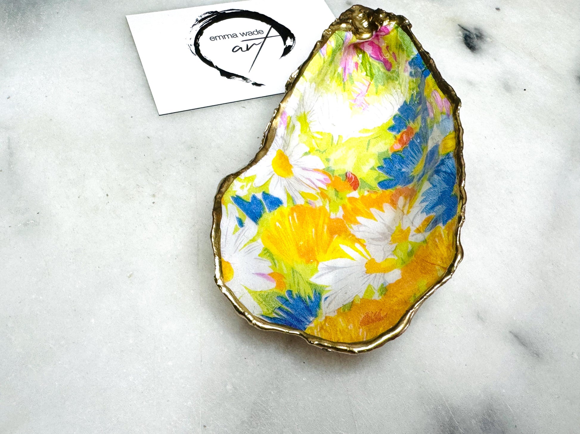 Handmade Dorset oyster shell trinket dish featuring colourful floral artwork in pink, yellow, orange, and blue tones with genuine gold leaf edging and glossy resin finish. Coastal jewellery holder and vibrant floral home décor gift.