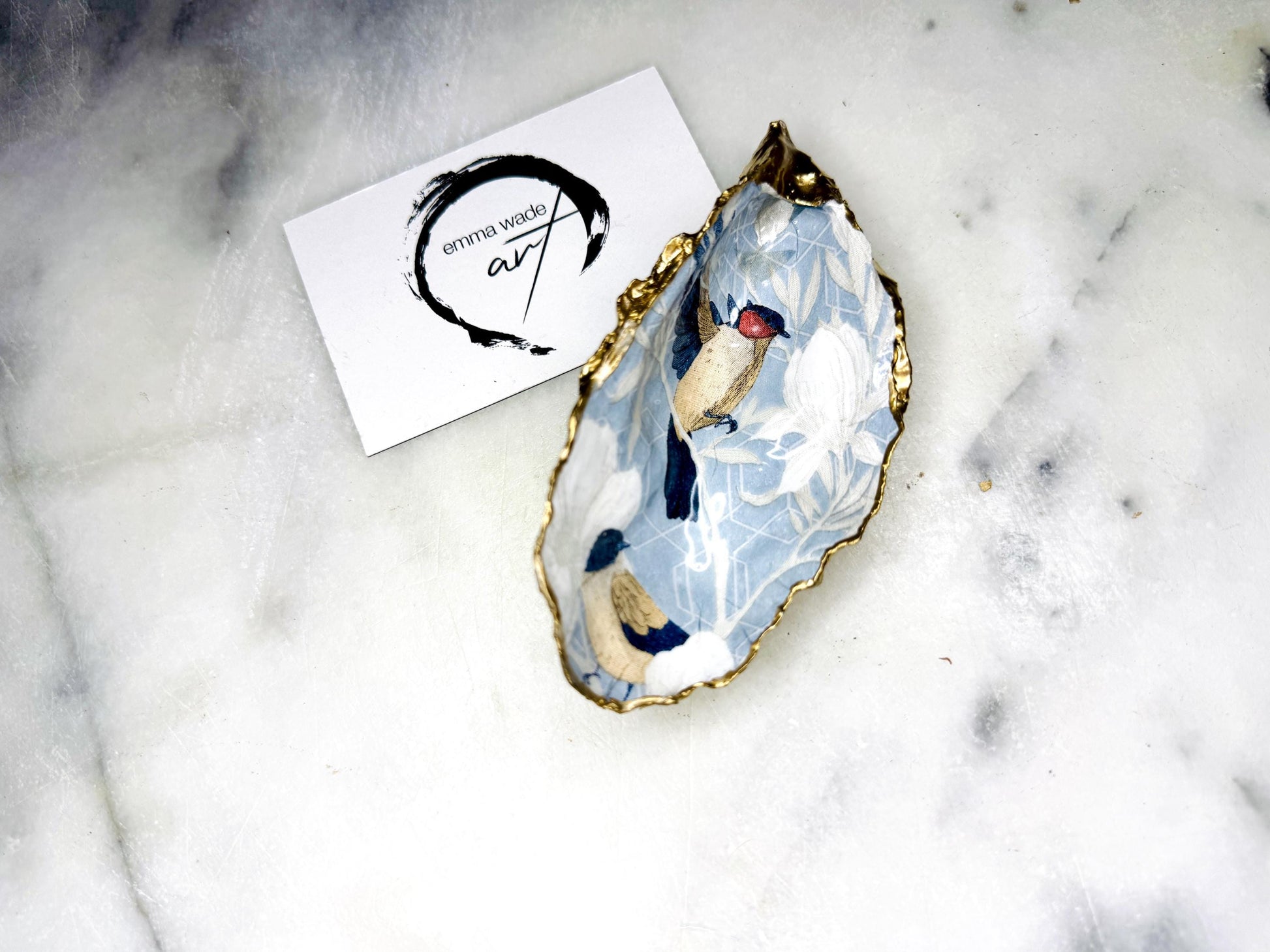 Handmade Dorset oyster shell trinket dish featuring elegant blue bird design with hand gilded gold leaf edging and glossy crystal clear resin finish, luxury coastal jewellery holder and decorative ring dish inspired by birds of paradise and coastal nature