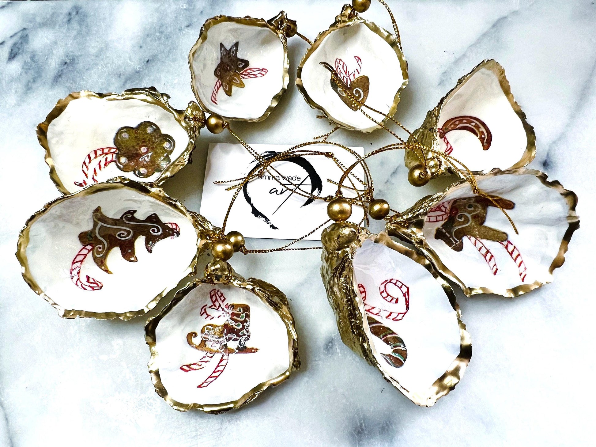 Handcrafted Dorset oyster shell Christmas ornaments featuring gingerbread-inspired festive motifs including candy canes, stars, moons, hearts, and skates. Gold leaf edged coastal Christmas baubles with glossy resin finish and pearl shell interiors displayed as luxury handmade holiday decorations.