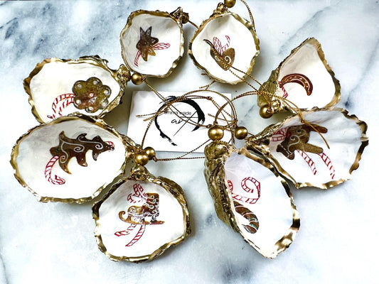 Handcrafted Dorset oyster shell Christmas ornaments featuring gingerbread-inspired festive motifs including candy canes, stars, moons, hearts, and skates. Gold leaf edged coastal Christmas baubles with glossy resin finish and pearl shell interiors displayed as luxury handmade holiday decorations.