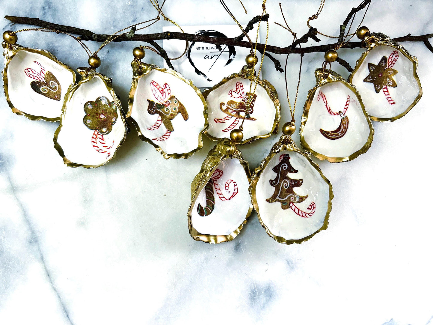 Handcrafted Dorset oyster shell Christmas ornaments featuring gingerbread-inspired festive motifs including candy canes, stars, moons, hearts, and skates. Gold leaf edged coastal Christmas baubles with glossy resin finish and pearl shell interiors displayed as luxury handmade holiday decorations.