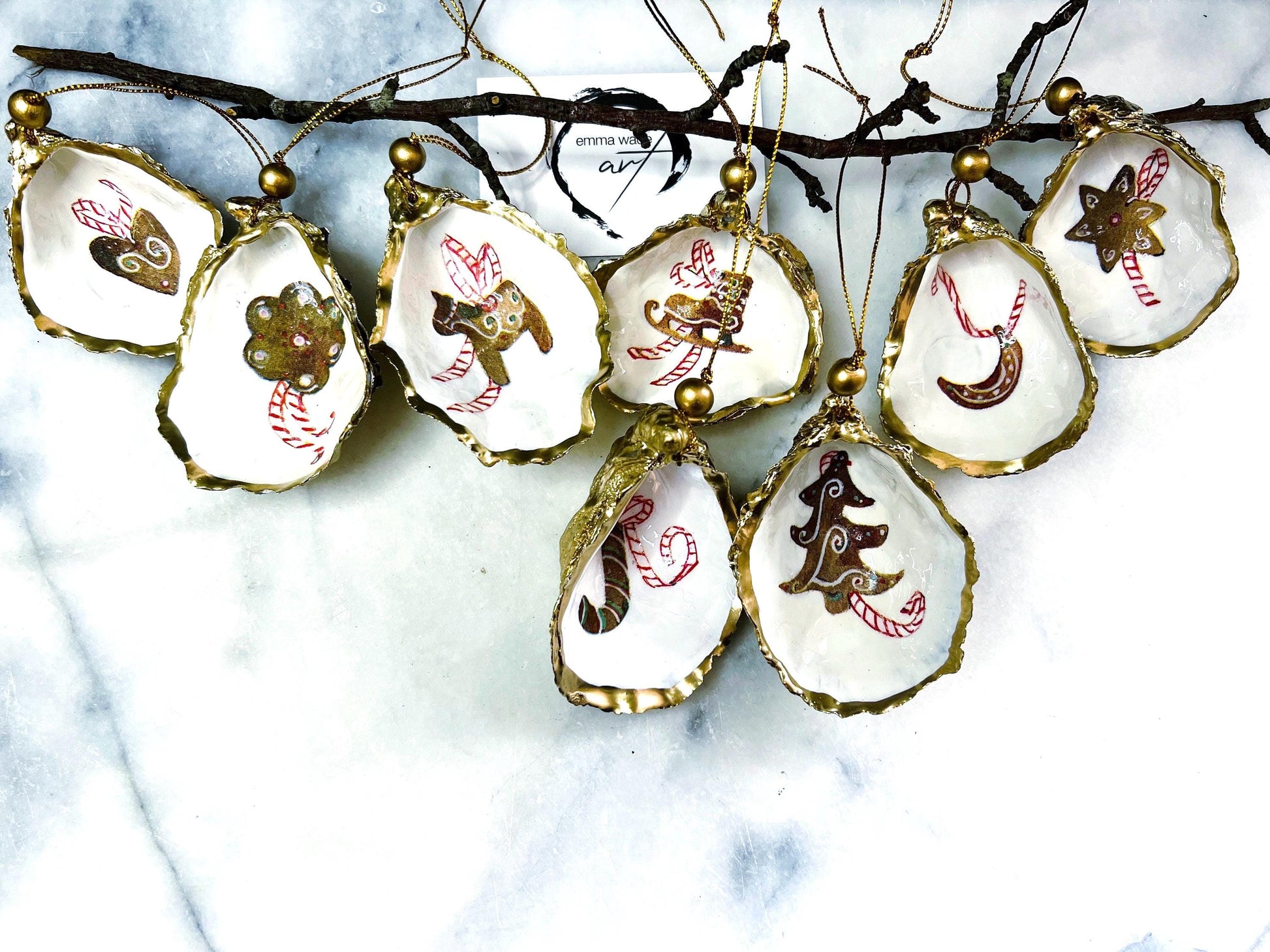 Handcrafted Dorset oyster shell Christmas ornaments featuring gingerbread-inspired festive motifs including candy canes, stars, moons, hearts, and skates. Gold leaf edged coastal Christmas baubles with glossy resin finish and pearl shell interiors displayed as luxury handmade holiday decorations.