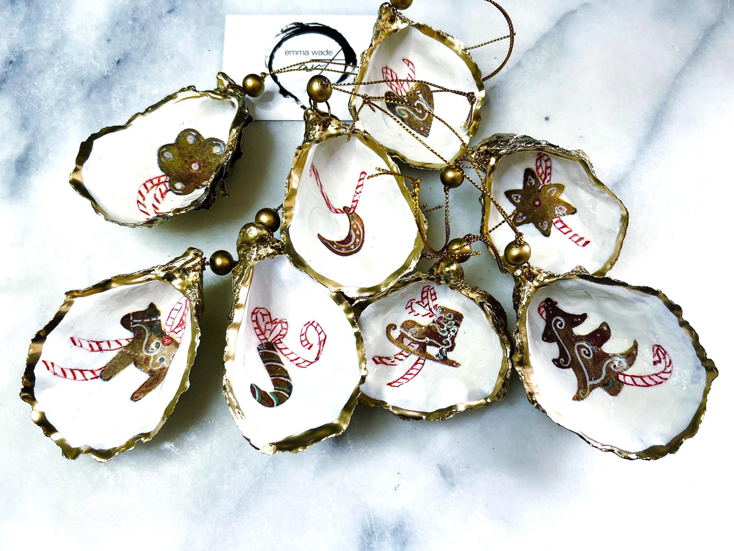 Handcrafted Dorset oyster shell Christmas ornaments featuring gingerbread-inspired festive motifs including candy canes, stars, moons, hearts, and skates. Gold leaf edged coastal Christmas baubles with glossy resin finish and pearl shell interiors displayed as luxury handmade holiday decorations.