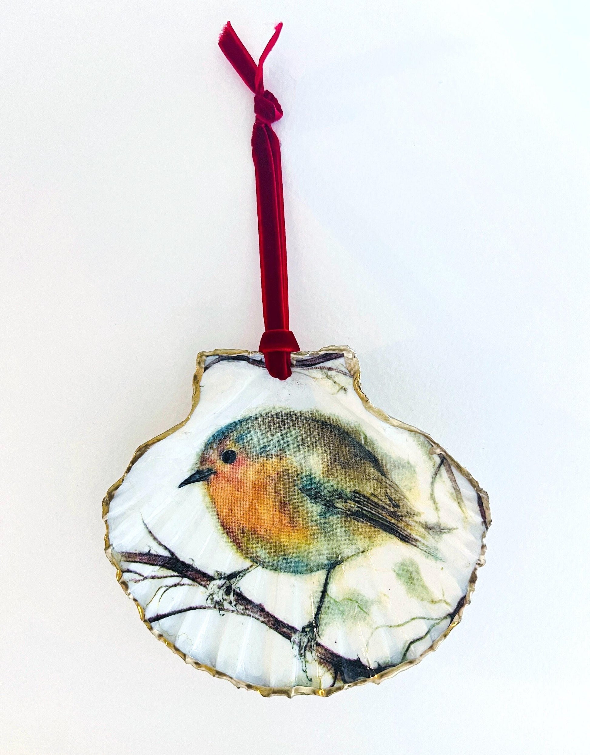 Handcrafted Dorset scallop shell trinket dish featuring a robin redbreast illustration with gold leaf edging and glossy resin finish. Coastal cottagecore jewellery holder and Christmas hanging ornament with natural shell texture and festive British bird design.