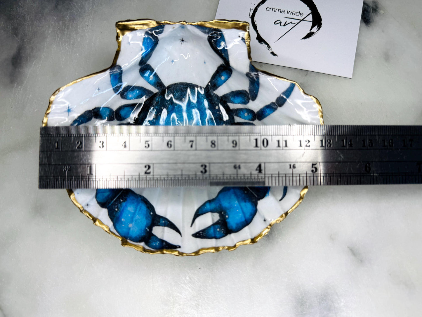 Scallop shell trinket dish with a hand drawn and hand painted blue crab design from original watercolour artwork. The artwork is applied as a decoupage print, then enhanced with painted detailing for a unique finish. Each shell is edged with liquid gold leaf and sealed with glossy resin. A handmade shell ring dish, jewellery organiser, or trinket tray for rings, earrings, or cufflinks. Perfect coastal decor or gift for weddings, anniversaries, birthdays, or Christmas.